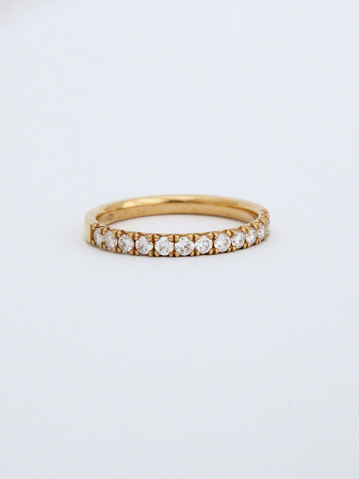 A yellow gold eternity ring featuring a row of round-cut diamonds, photographed on a clean white background.