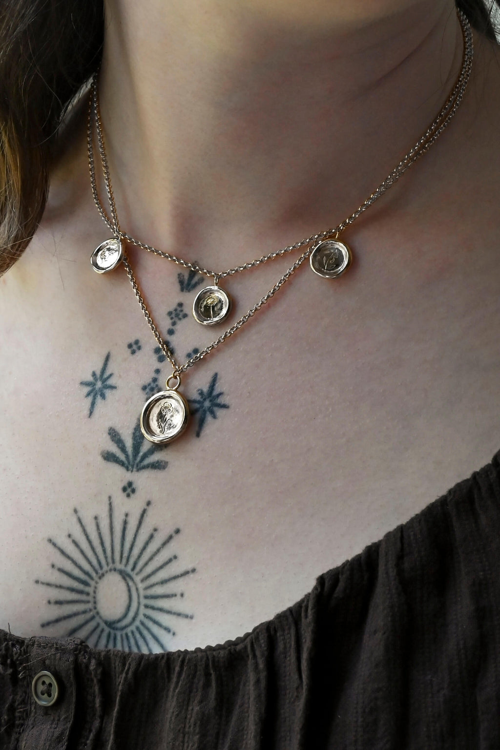 A silver choker chain and pendant necklace featuring three round medallion pendants with unique birth flower hand engraving on a woman's neck with tattoos.