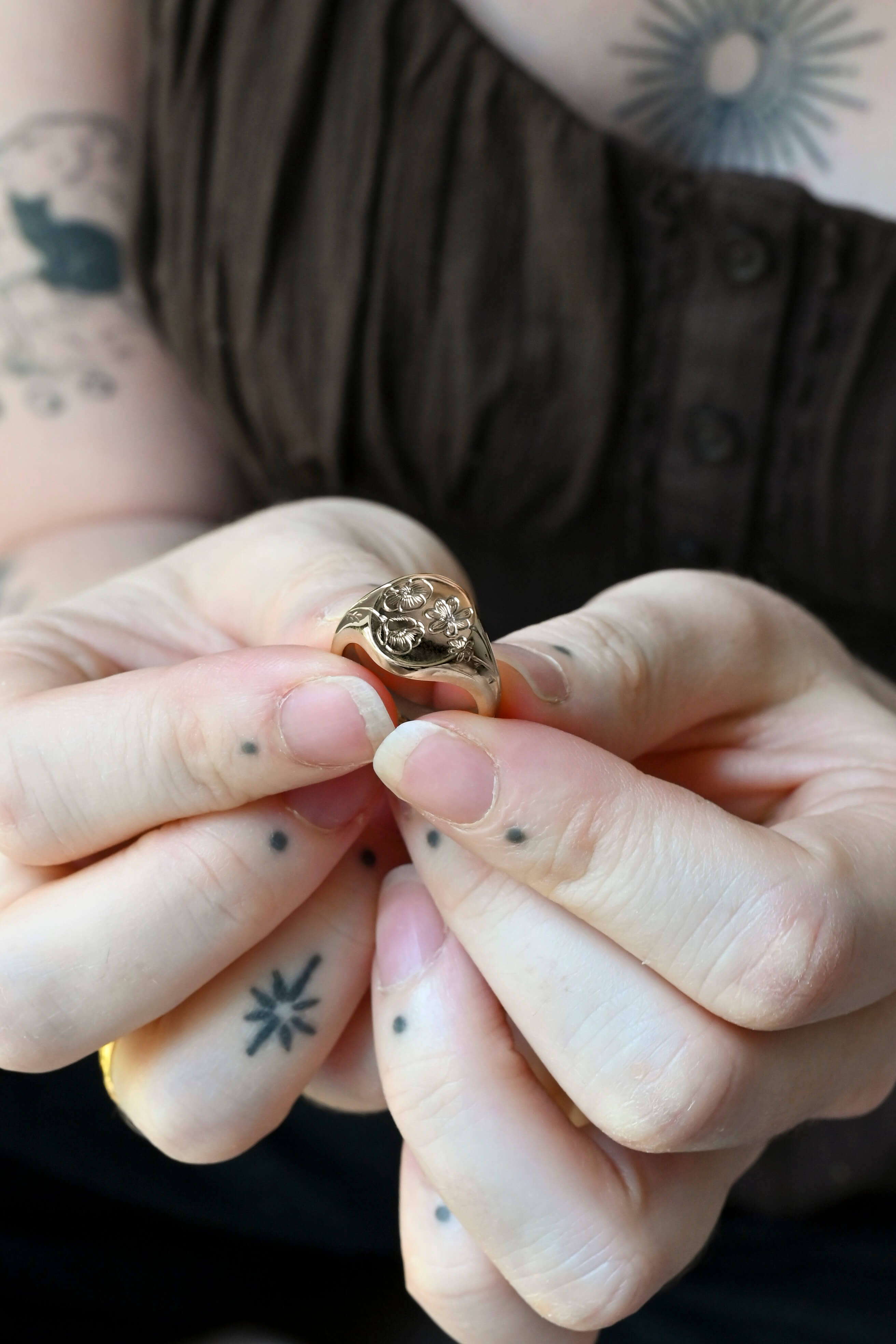 A unique silver signet ring with bespoke birth flower engraved design, held by a woman with tattoos.