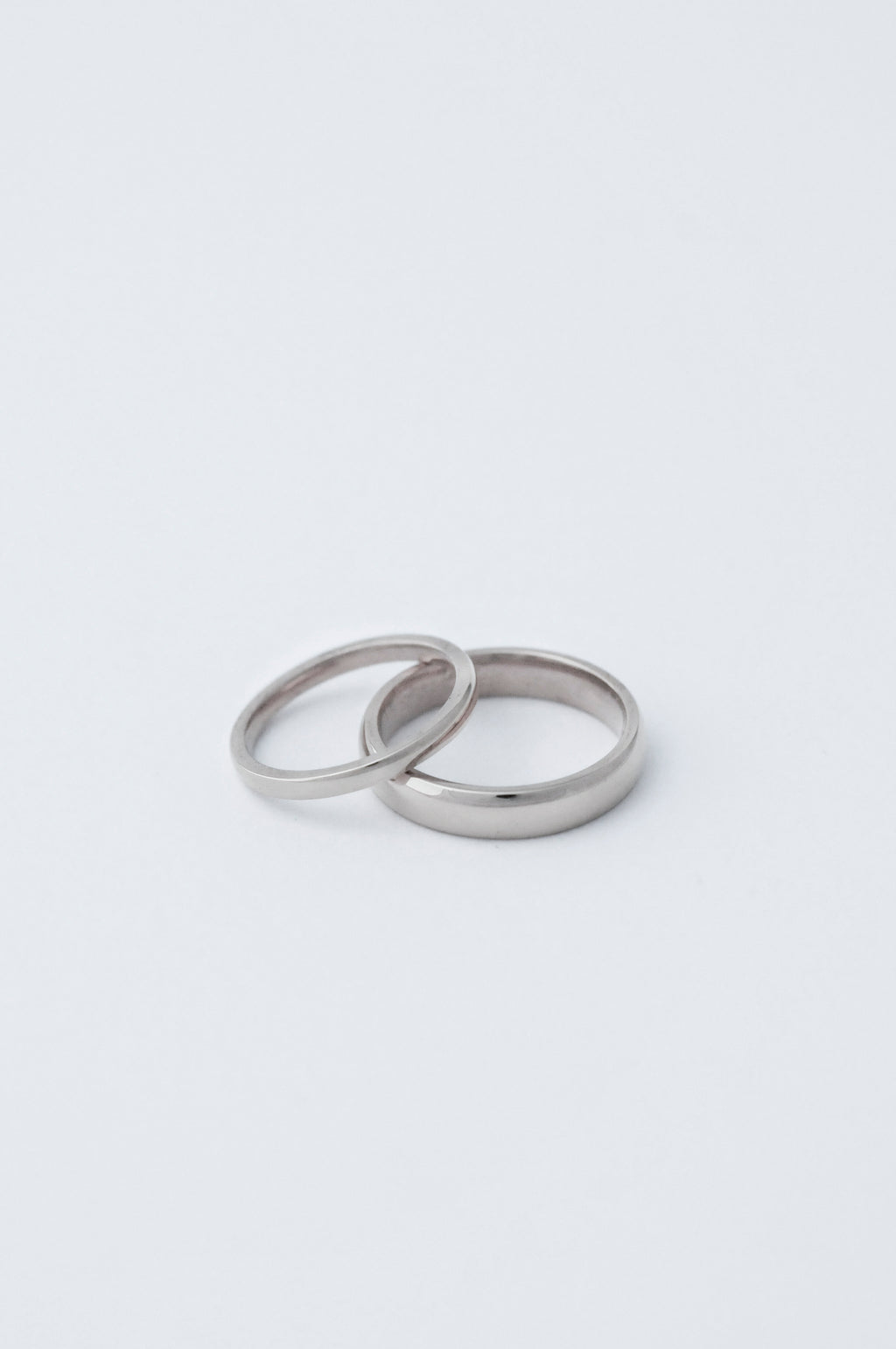 Two minimalist platinum wedding bands, both with a flat face, one s 2mm the other 5mm resting on a clean white surface.