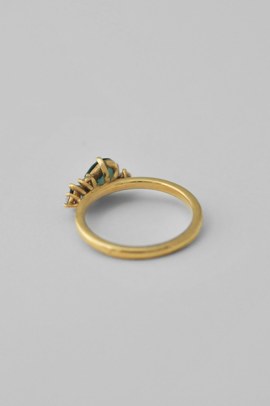 A gold ring with a small cluster of green gemstones, photographed on a neutral gray background.