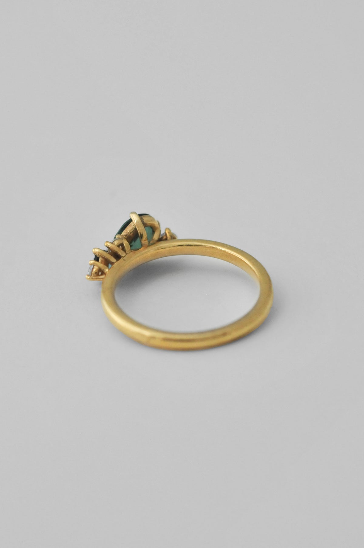 A gold ring with a small cluster of green gemstones, photographed on a neutral gray background.