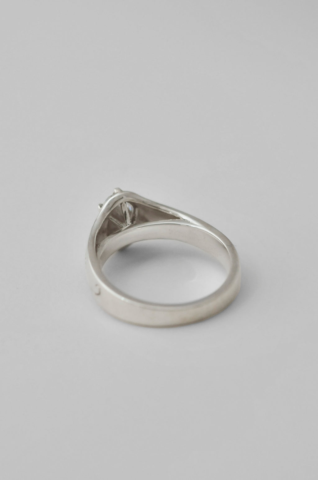 A silver signet ring showing the inside of the ring. diamond setting can be seen as the ring band, shown against a neutral light gray background.