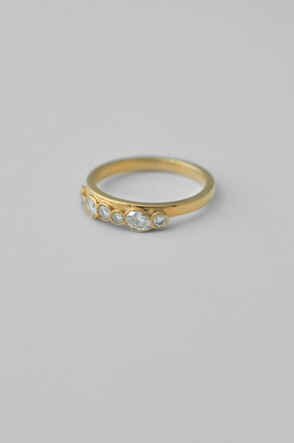 A gold ring with five bezel-set clear oval diamonds, photographed on a neutral light gray background.