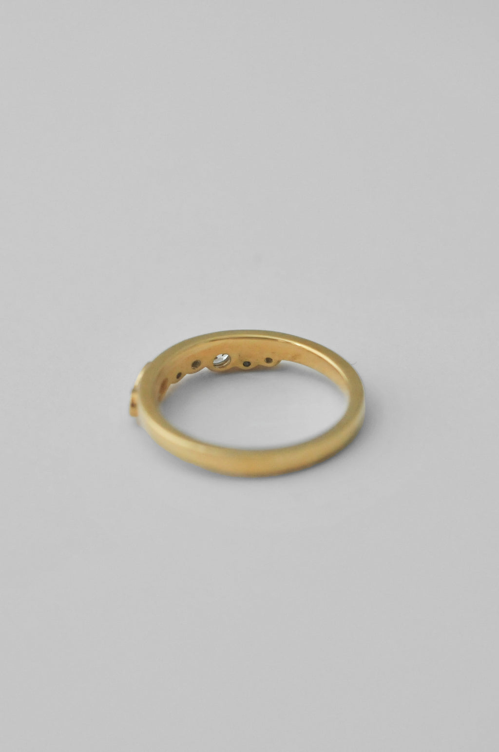 A gold band ring with a small central clear gemstone and three small side stones, photographed on a plain light gray background.
