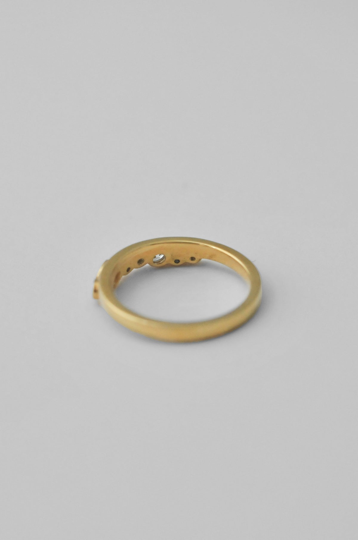 A gold band ring with a small central clear gemstone and three small side stones, photographed on a plain light gray background.