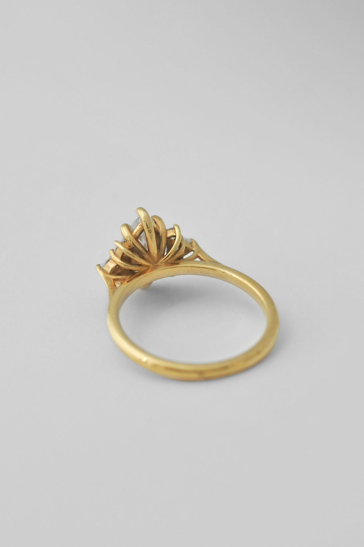 A yellow gold ring with a sculptural, fan-like floral crown setting, displaying the inside of the solitaire ring photographed on a neutral light gray background.