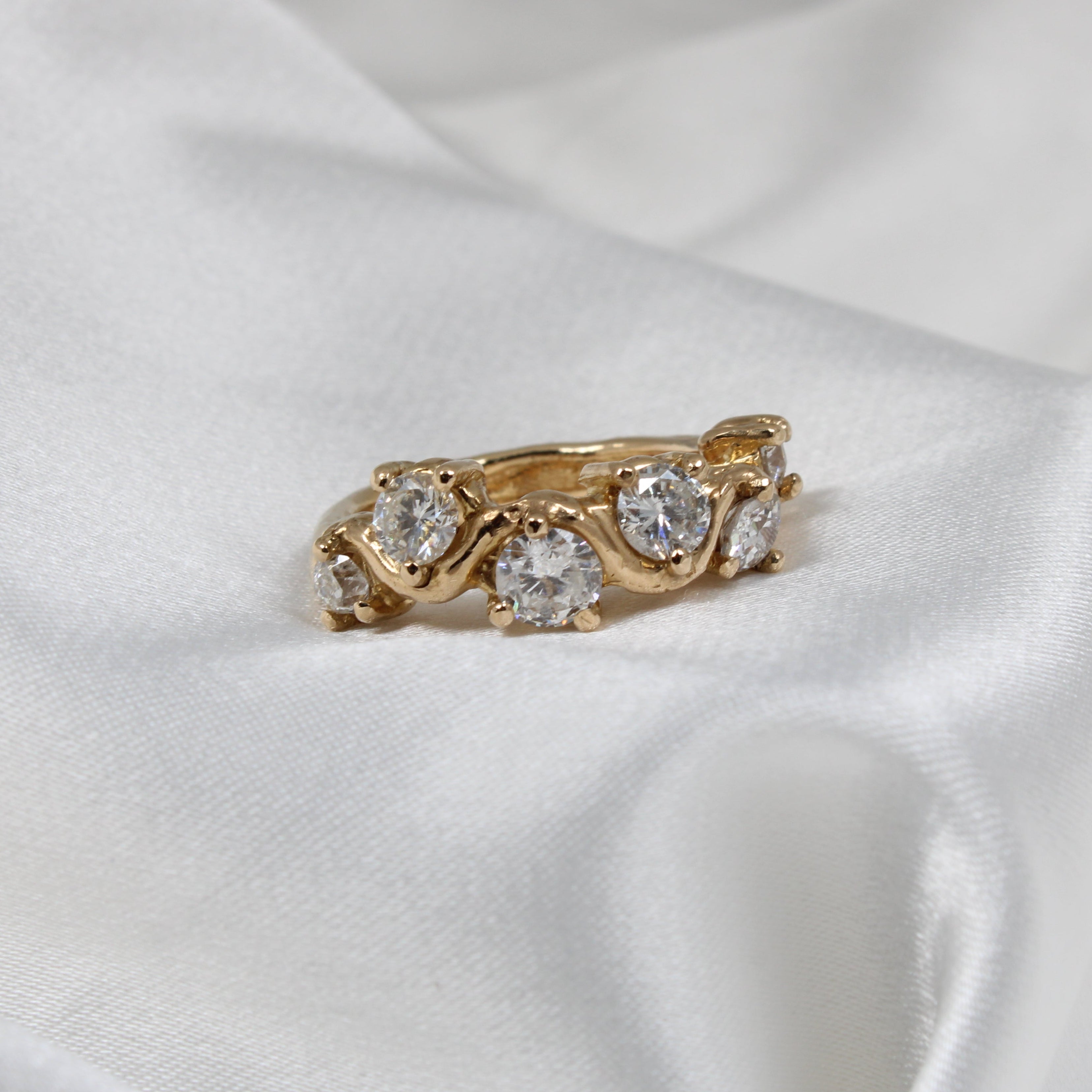 Organic gold ring with diamonds on a white satin background