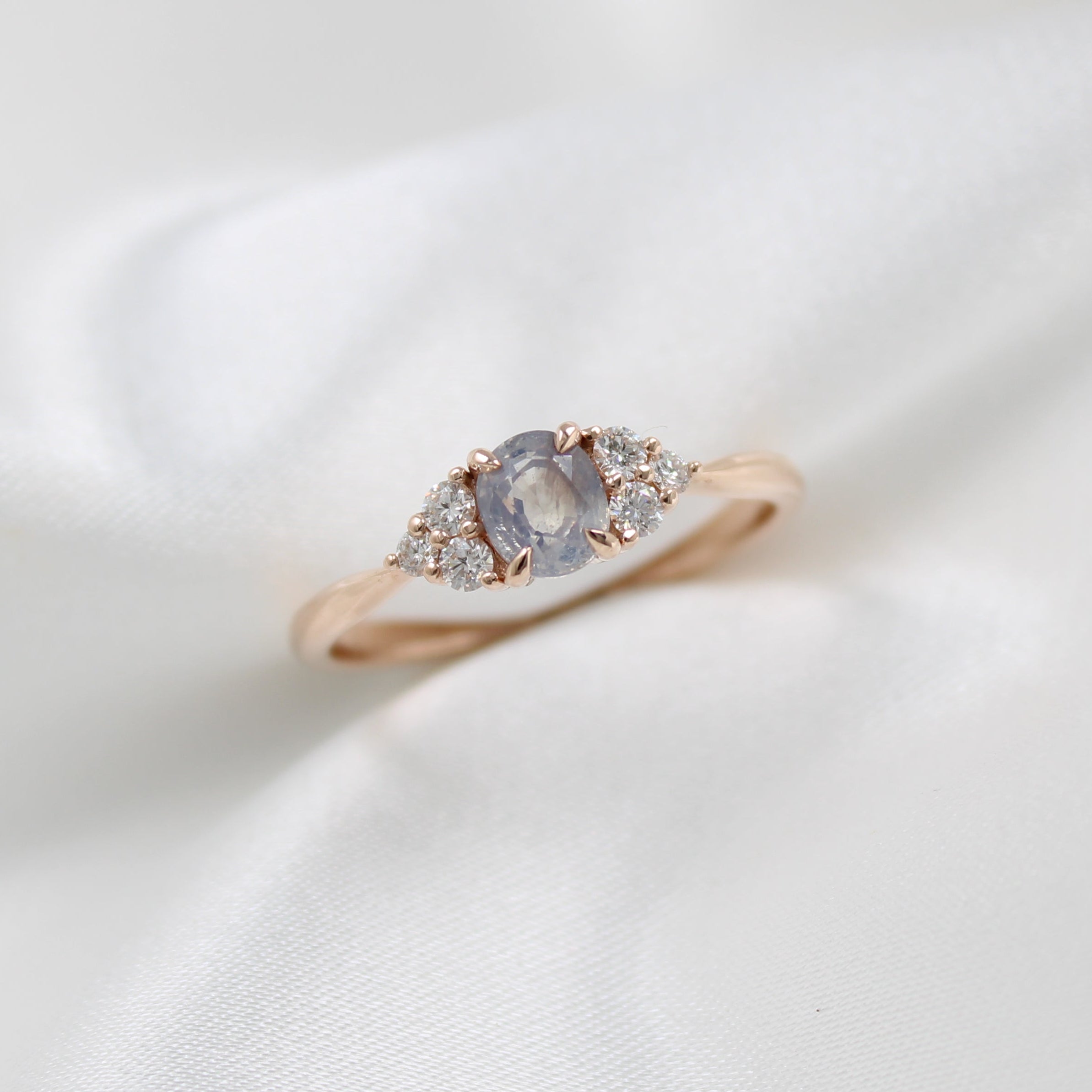 Rose gold ring with a central grey diamond and smaller stones on a white fabric background