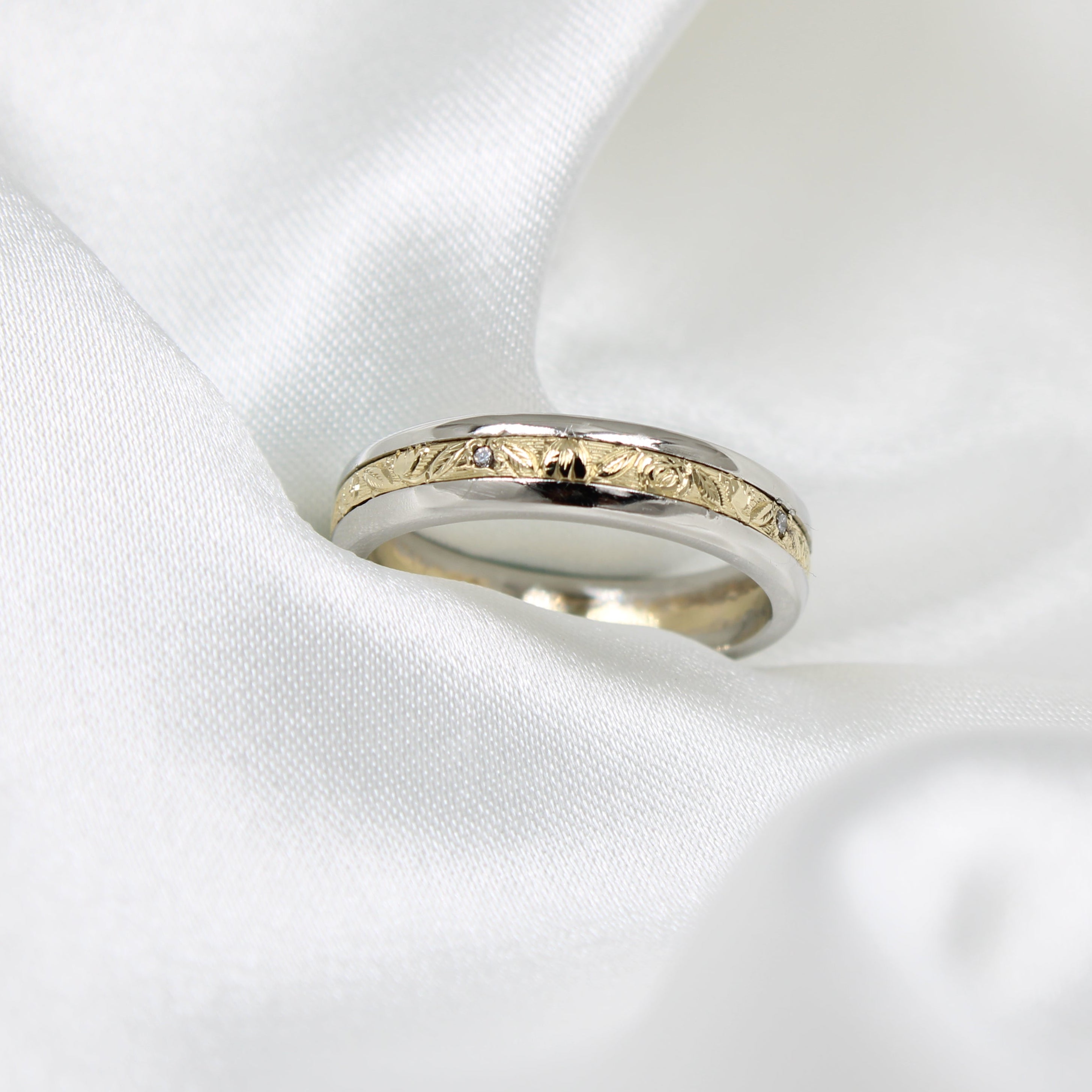 mixed metal white and yellow Gold engraved men's engagement ring on a white satin background