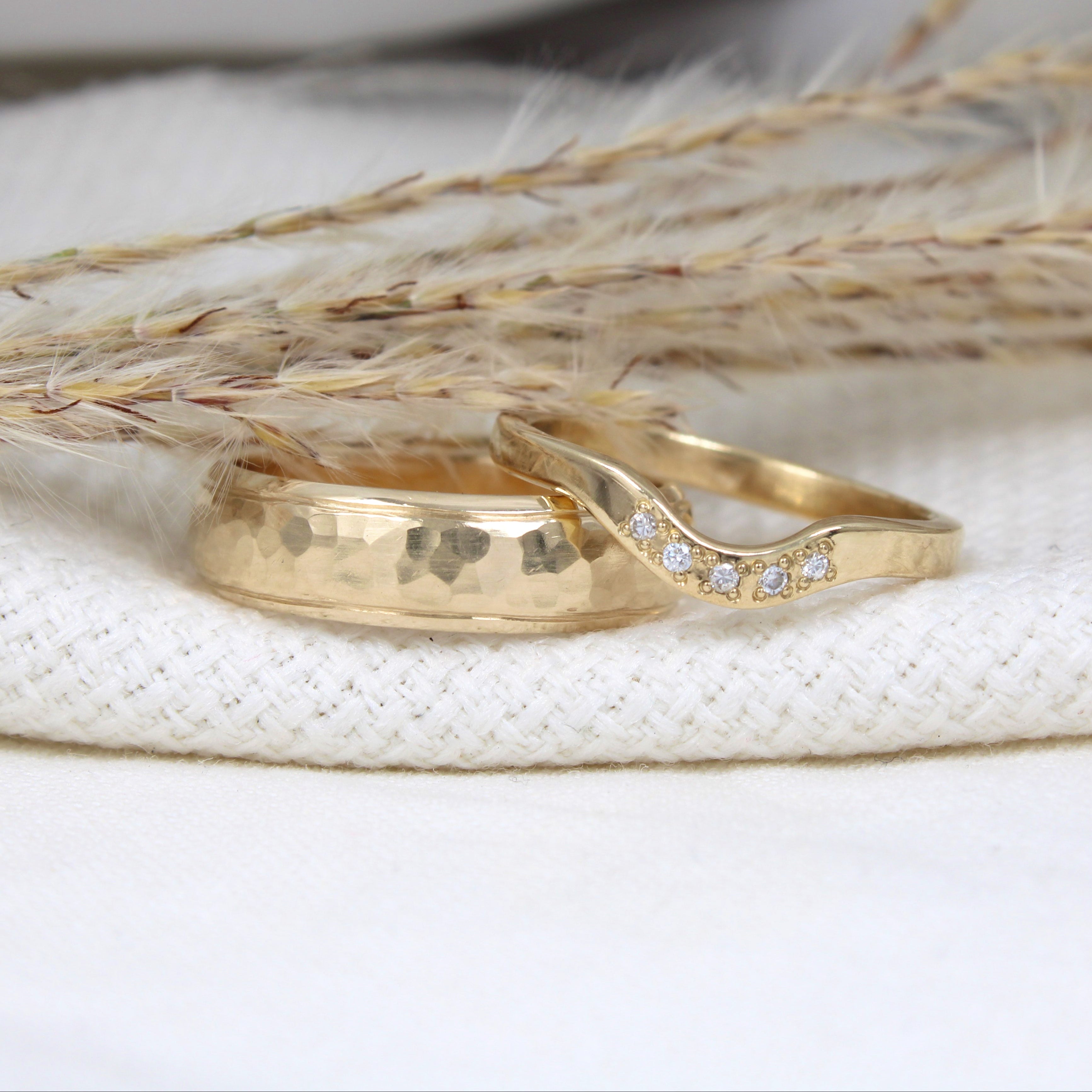 Solid gold his and hers hammered wedding bands with diamonds on natural background