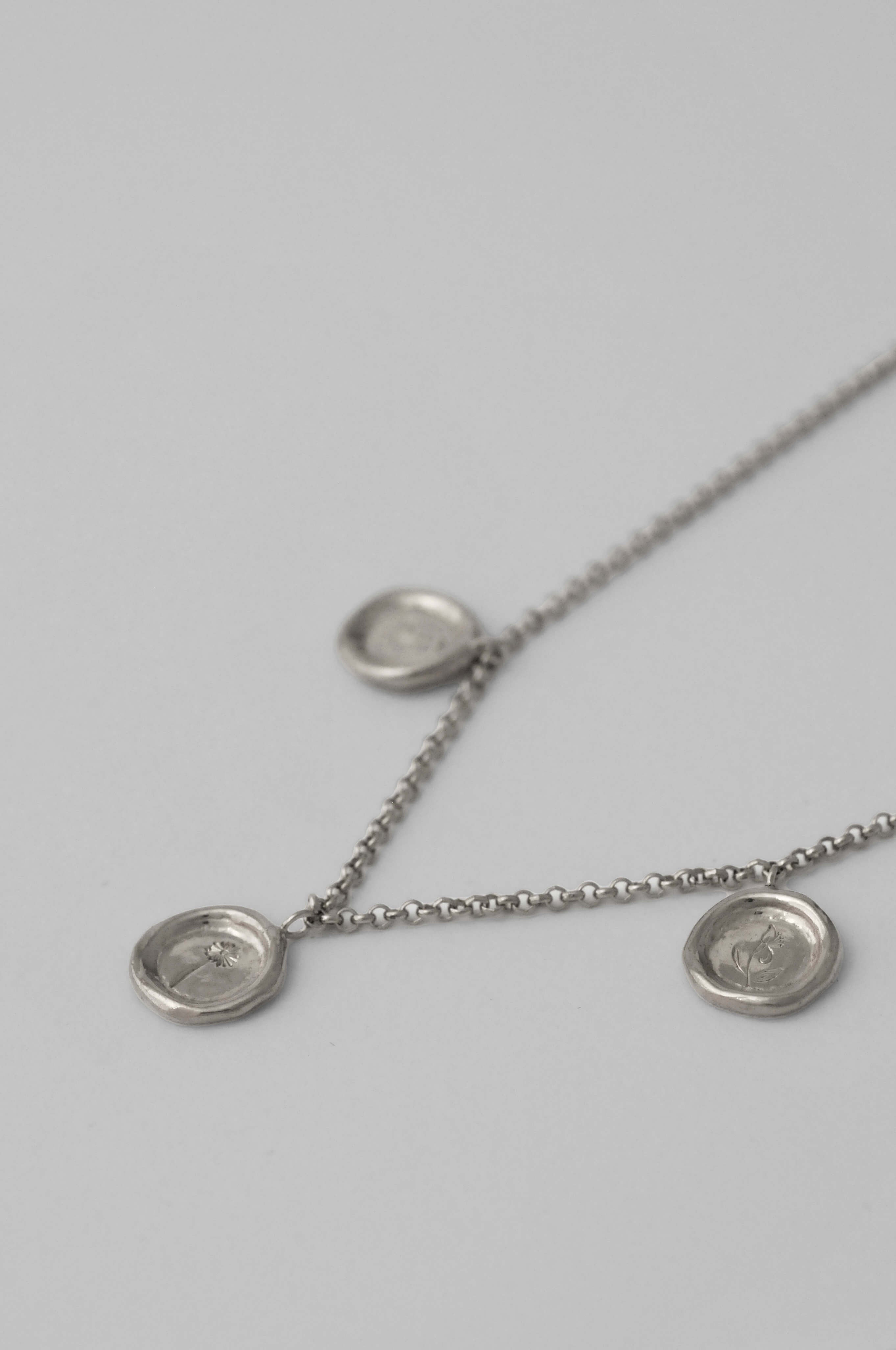 A silver choker chain necklace featuring three round coin-like pendants with three bespoke birth flower hand engraving displayed against a light gray background.