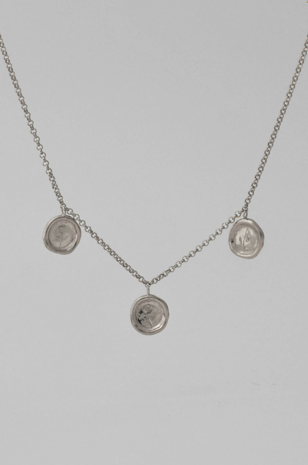 A silver choker chain necklace featuring three round medallion pendants with personalised birth flower hand engraving displayed against a light gray background.