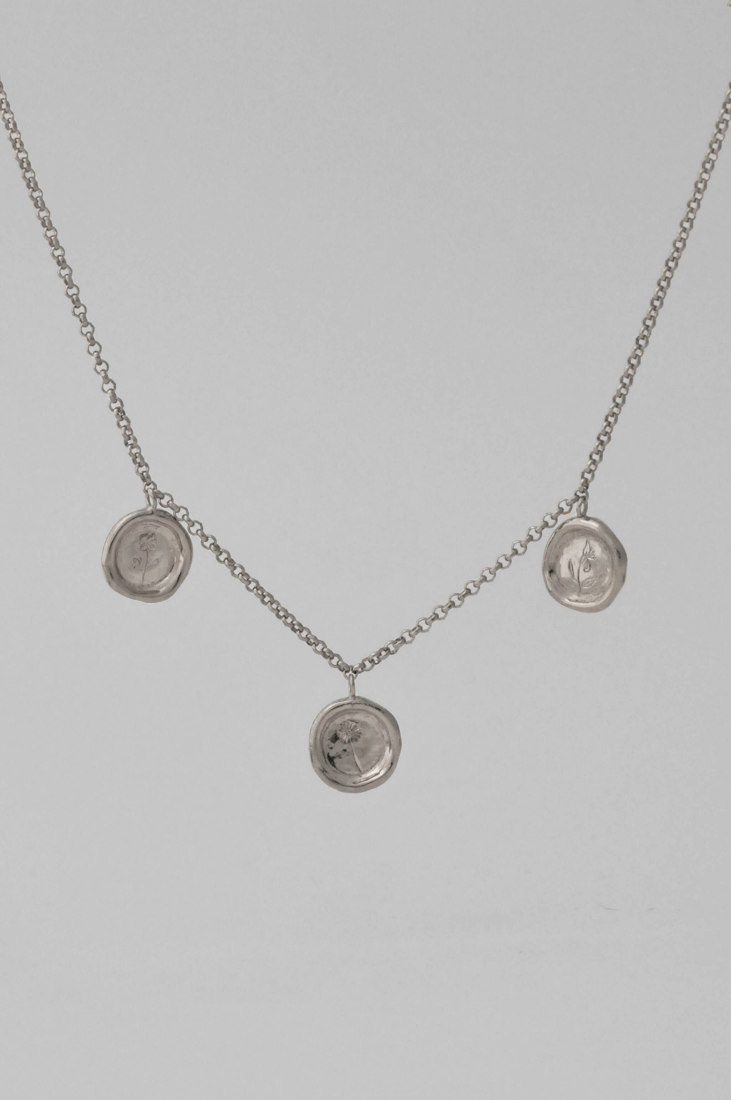 A silver choker chain necklace featuring three round medallion pendants with personalised birth flower hand engraving displayed against a light gray background.