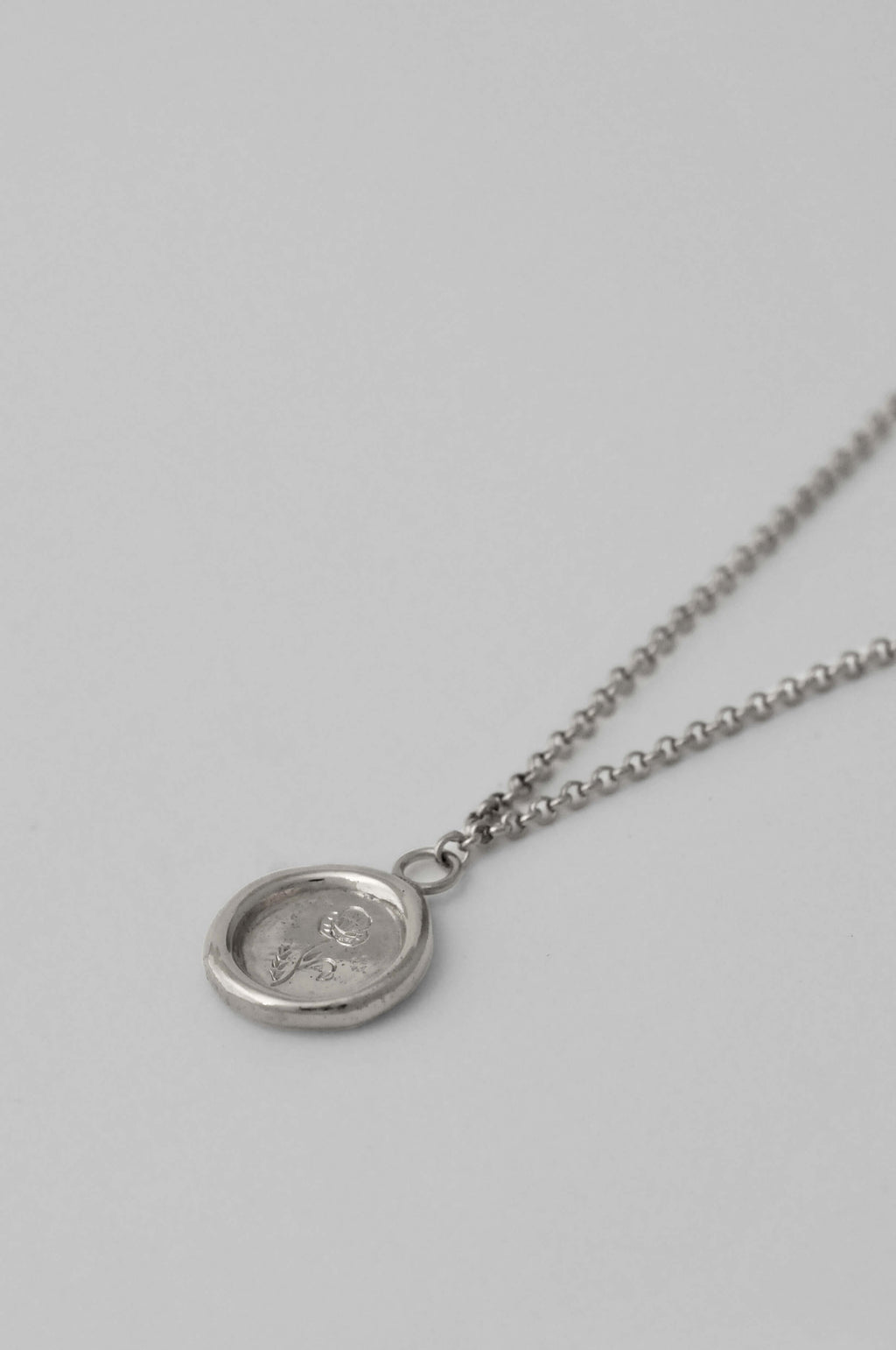 A silver necklace with a chunky organic wax-seal medallion pendant featuring birth flower hand engraved resting on a white background.