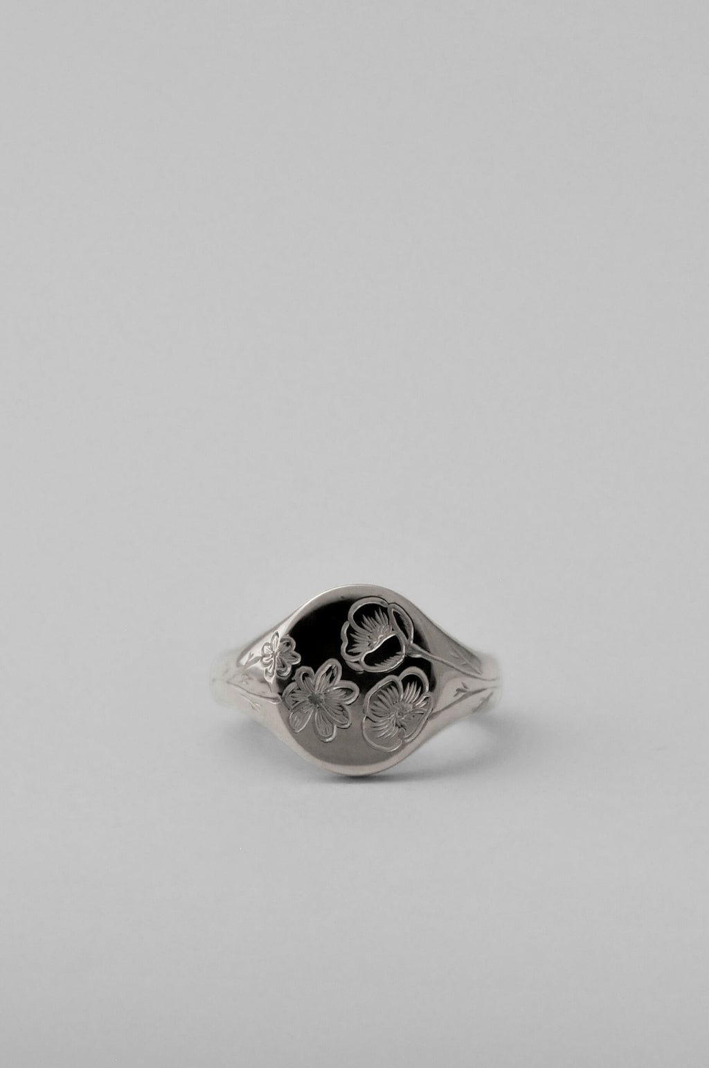 A classic silver signet ring with engraved floral birth flower motifs, shown on a neutral light grey background.