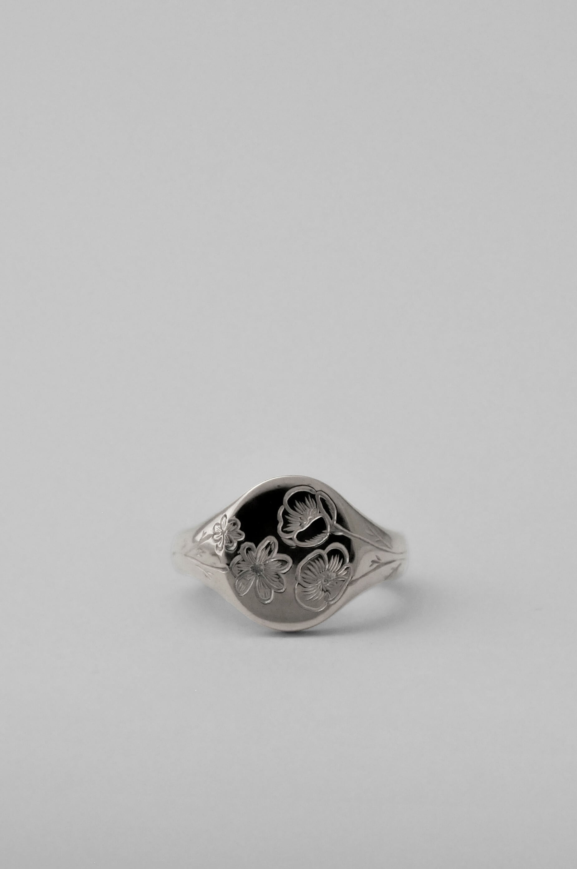 A classic silver signet ring with engraved floral birth flower motifs, shown on a neutral light grey background.