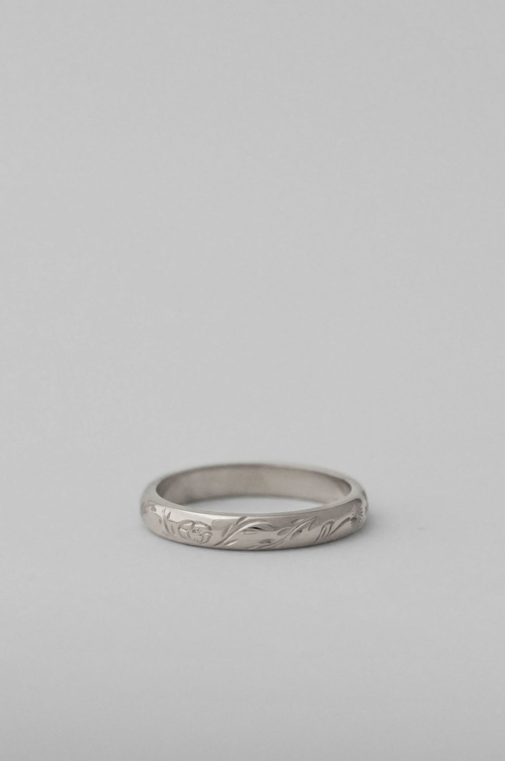 A silver band ring with a hand engraved floral pattern, photographed on a neutral white background.