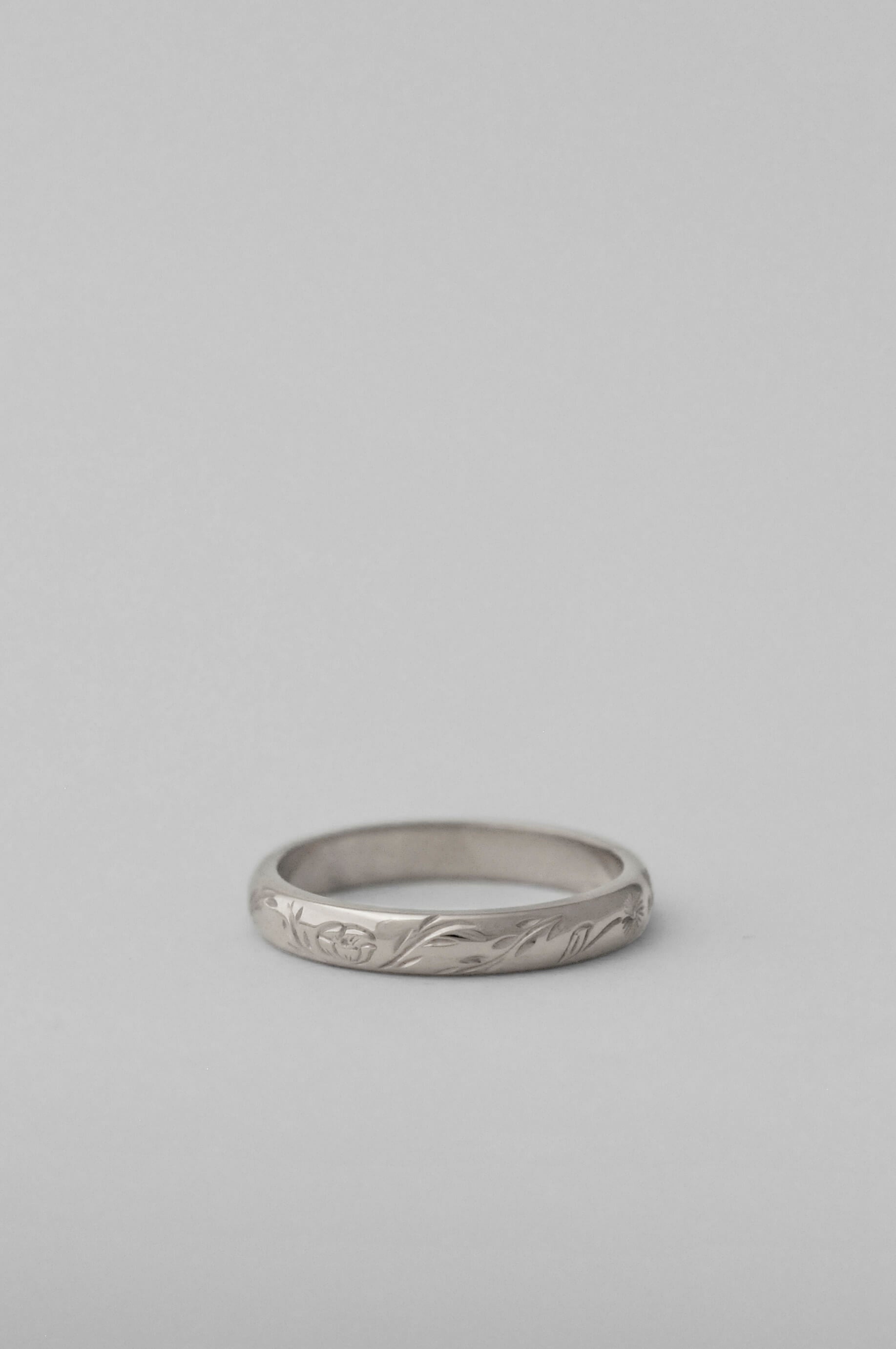 A silver band ring with a hand engraved floral pattern, photographed on a neutral white background.