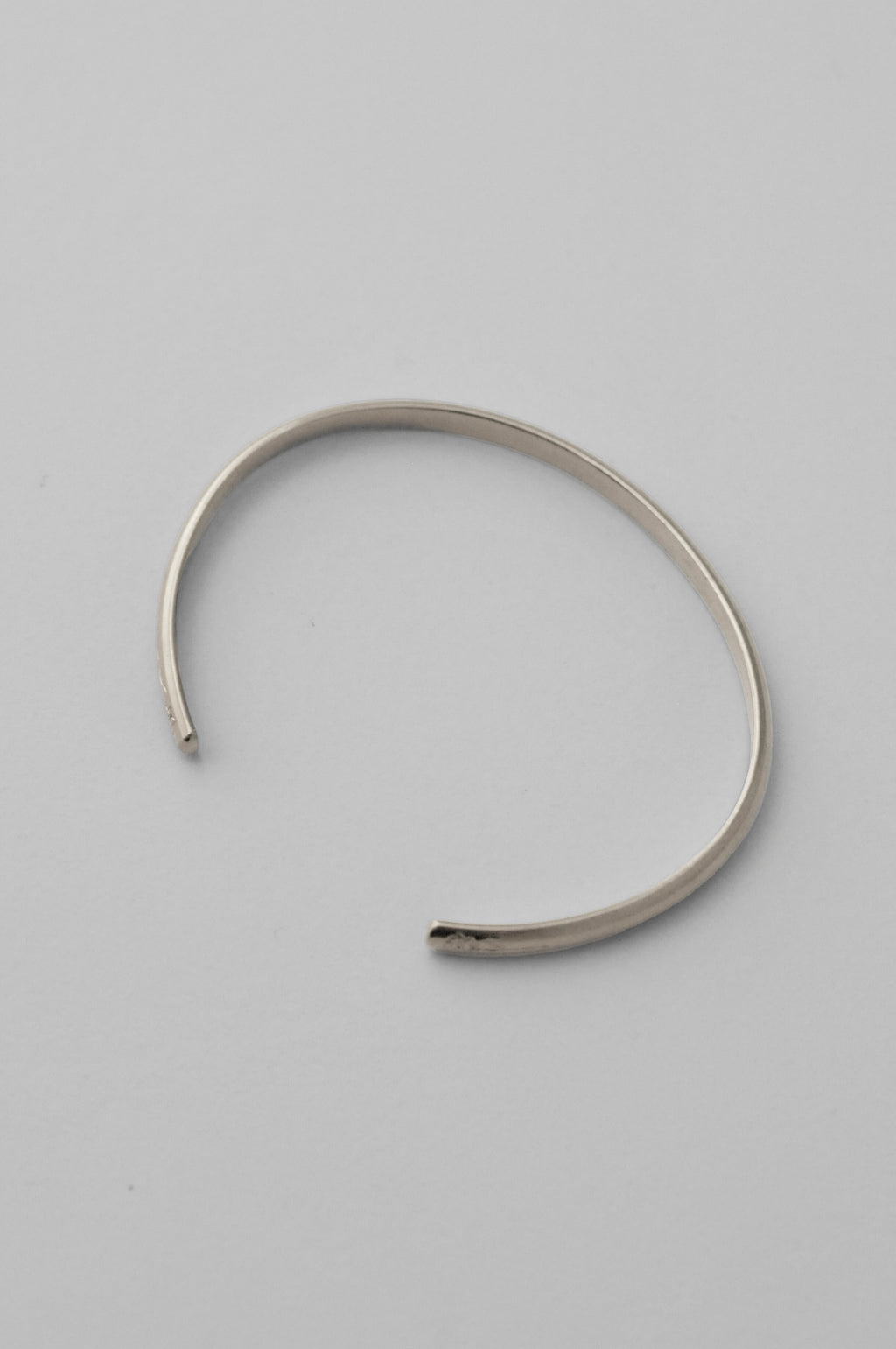 A minimalist sterling silver open cuff bangle bracelet with hand engraved flowers on each end, photographed on a clean, white background.