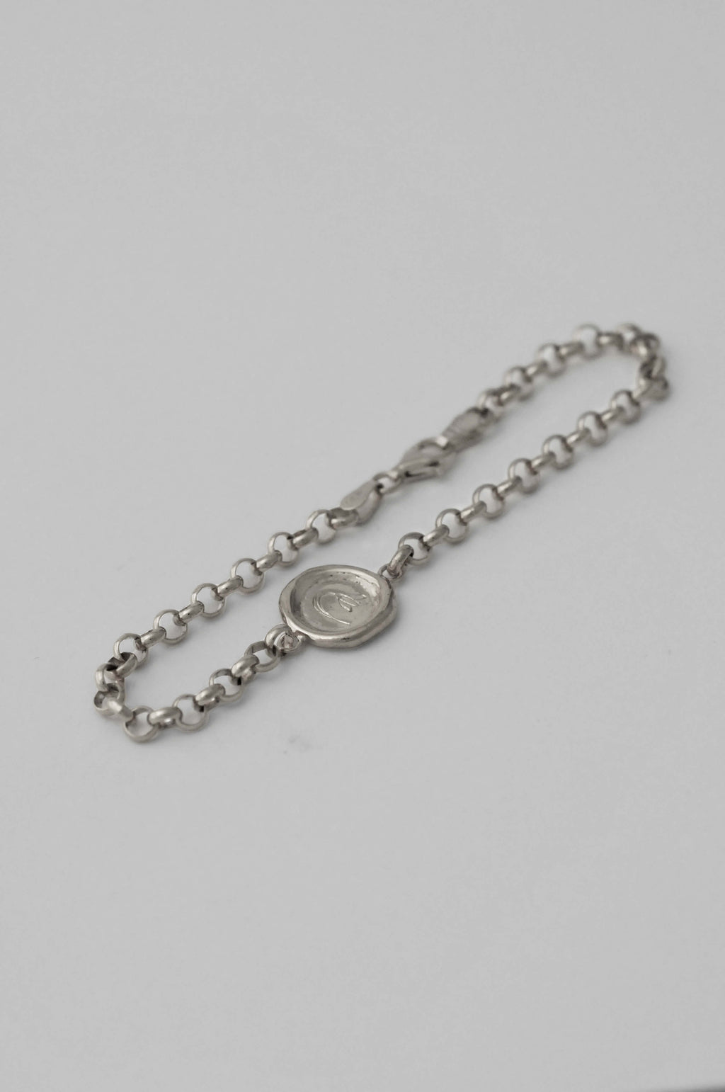 A silver chain bracelet with a round medallion pendant with hand engraved flower, displayed on a natural white background.