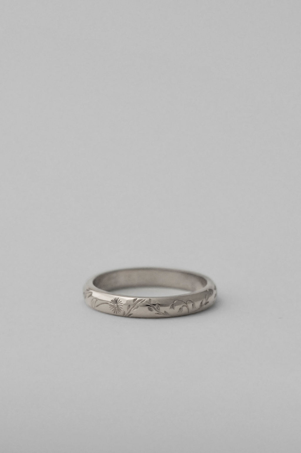 A silver band ring with delicate hand engraved florals, photographed on a neutral white background.