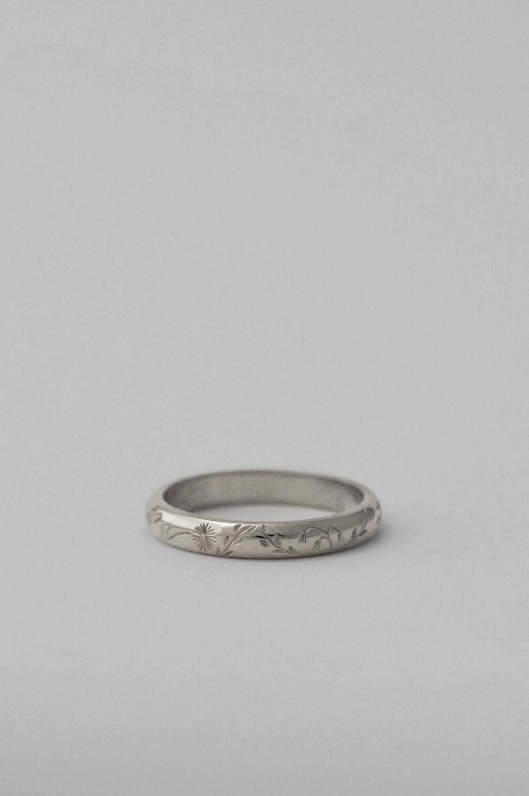 A silver band ring with delicate hand engraved florals, photographed on a neutral white background.