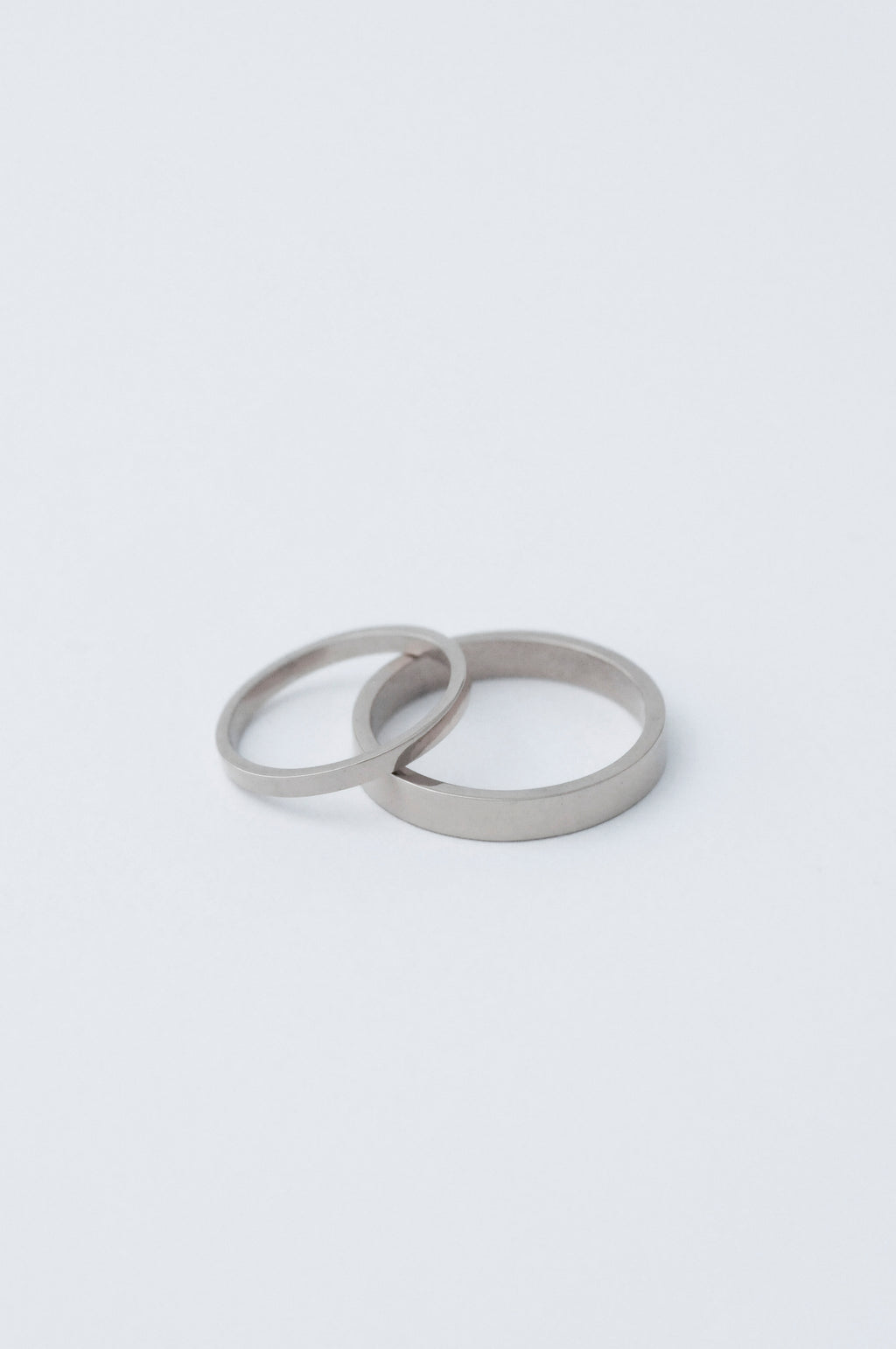 Two minimalist platinum wedding bands, both with a flat face, one s 2mm the other 5mm resting on a clean white surface.