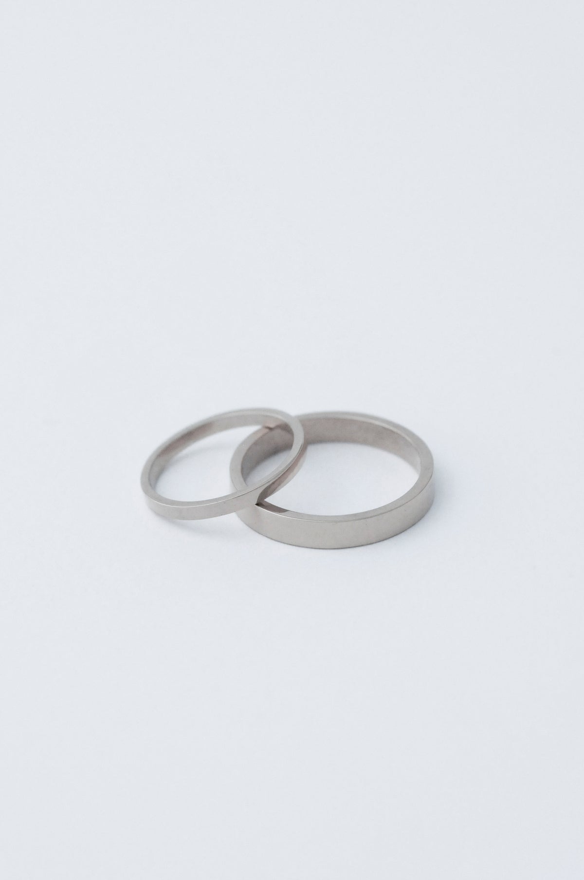 Two minimalist platinum wedding bands, both with a flat face, one s 2mm the other 5mm resting on a clean white surface.