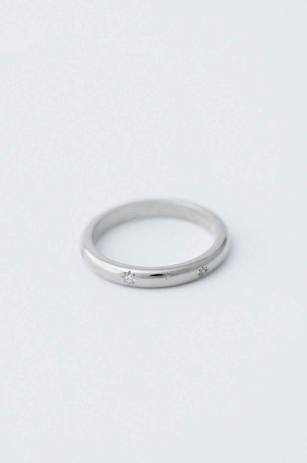 A thin platinum ring with a small star-shaped diamond set in the centre, photographed on a clean, light gray background.