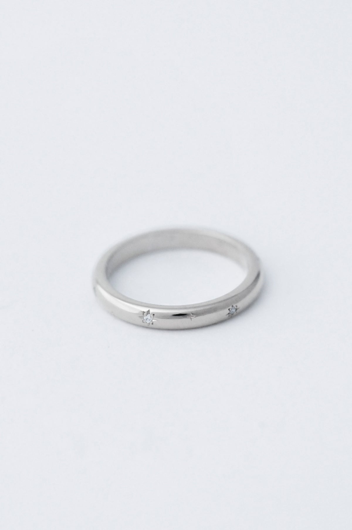 A thin platinum ring with a small star-shaped diamond set in the centre, photographed on a clean, light gray background.
