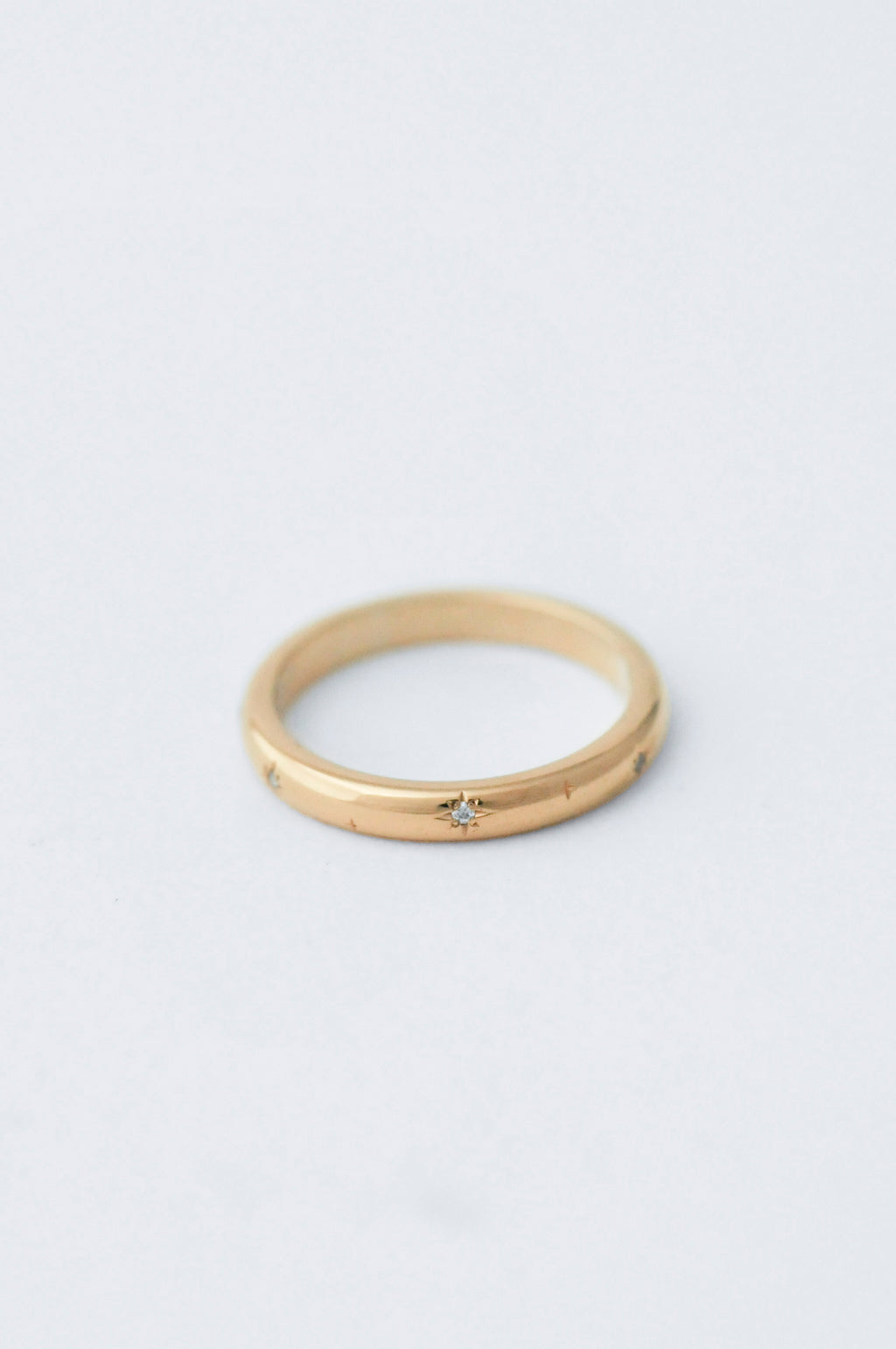 A thin yellow gold ring with a small star-shaped diamond set in the center, photographed on a clean, light gray background.