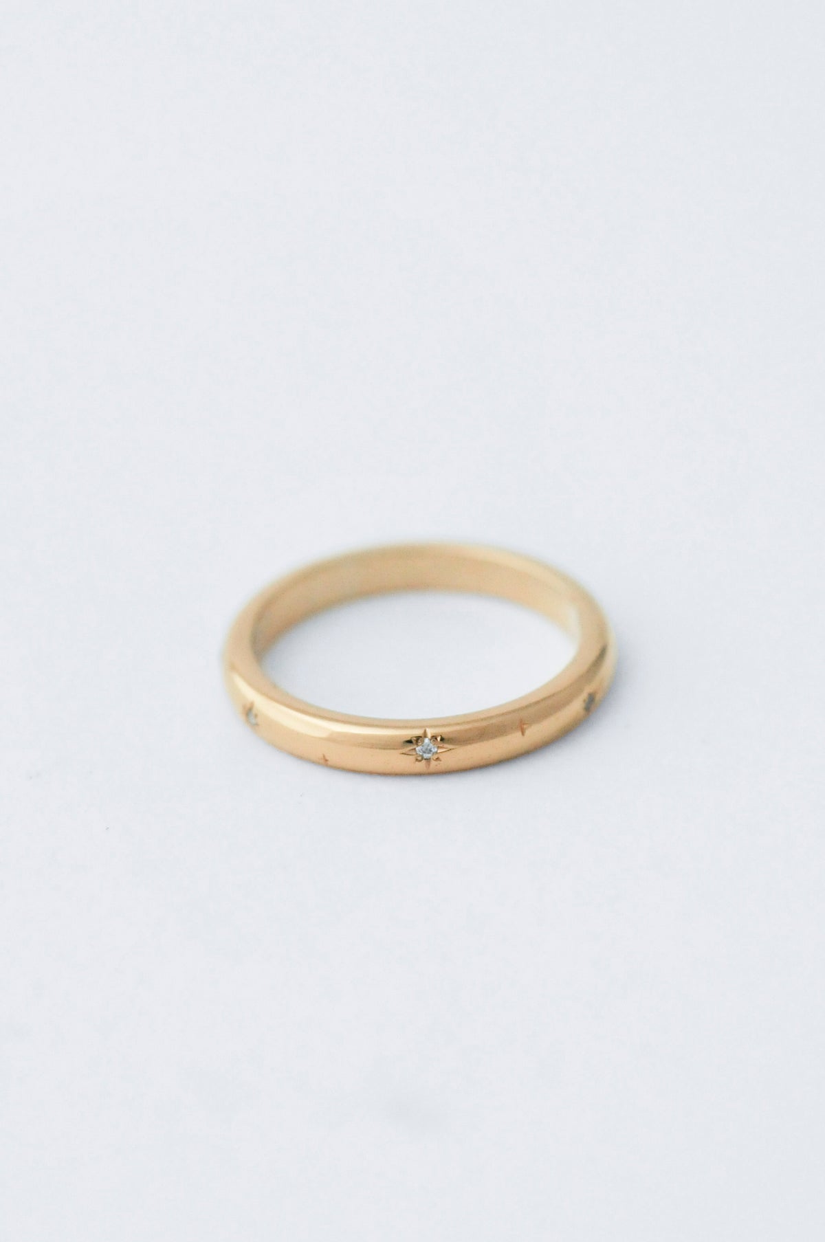 A thin yellow gold ring with a small star-shaped diamond set in the center, photographed on a clean, light gray background.