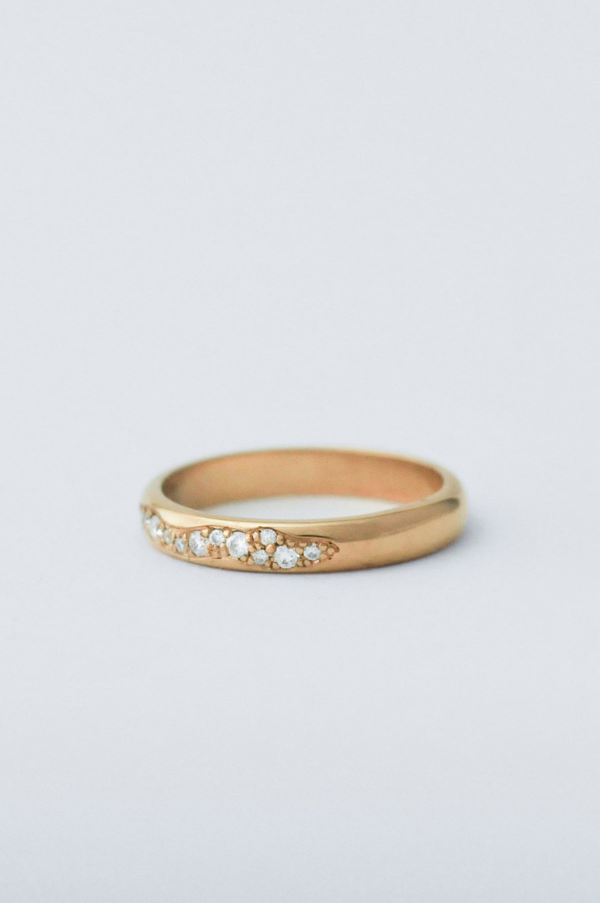 A gold band ring featuring a row of small diamonds along the front, photographed on a clean light gray background.