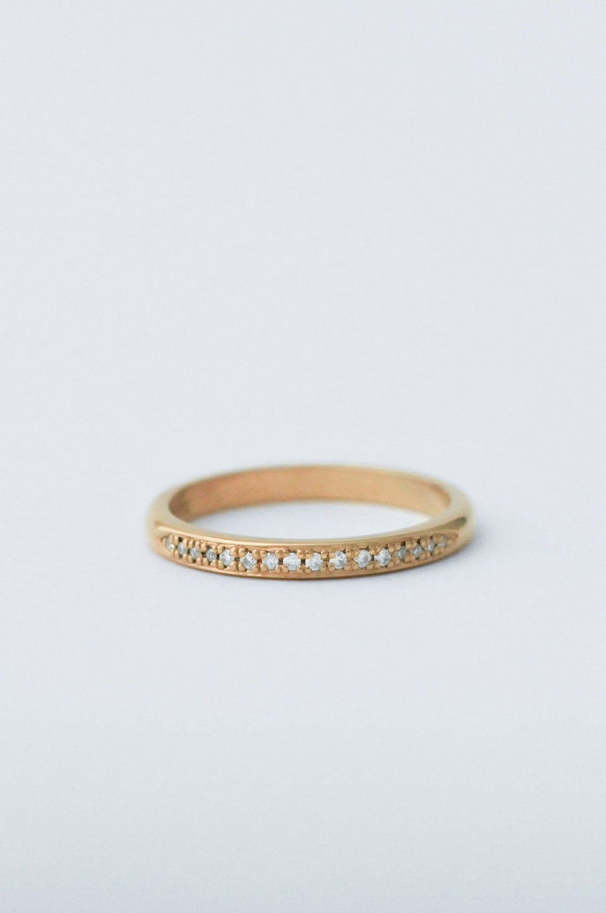 A delicate yellow gold ring featuring a row of small clear pavé-set diamonds along the front, photographed on a clean, light gray background.