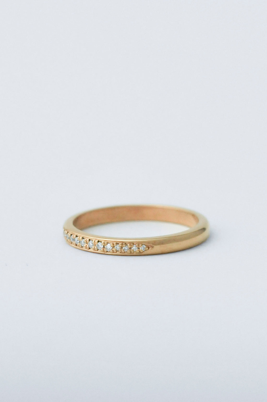 A thin yellow gold eternity ring with a row of small clear pavé-set diamonds along the front, photographed on a clean white background.