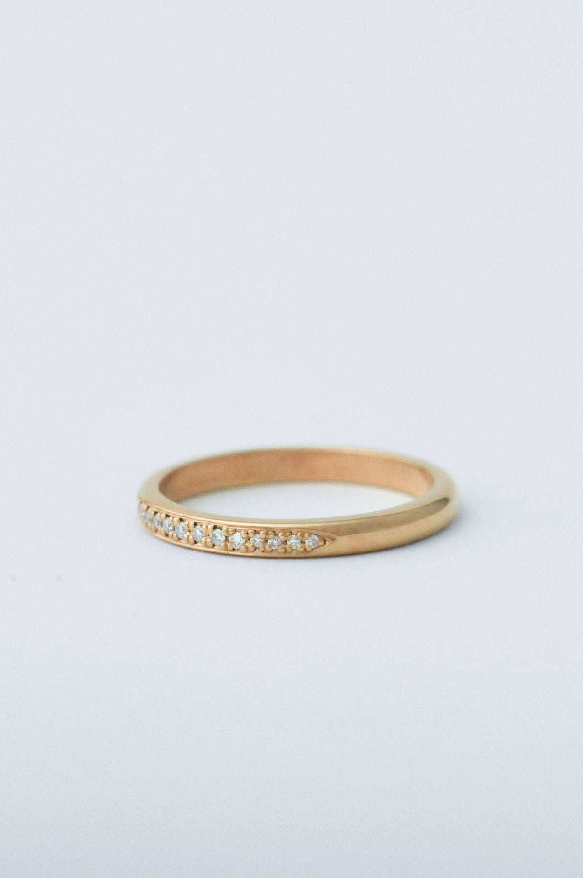 A thin yellow gold eternity ring with a row of small clear pavé-set diamonds along the front, photographed on a clean white background.