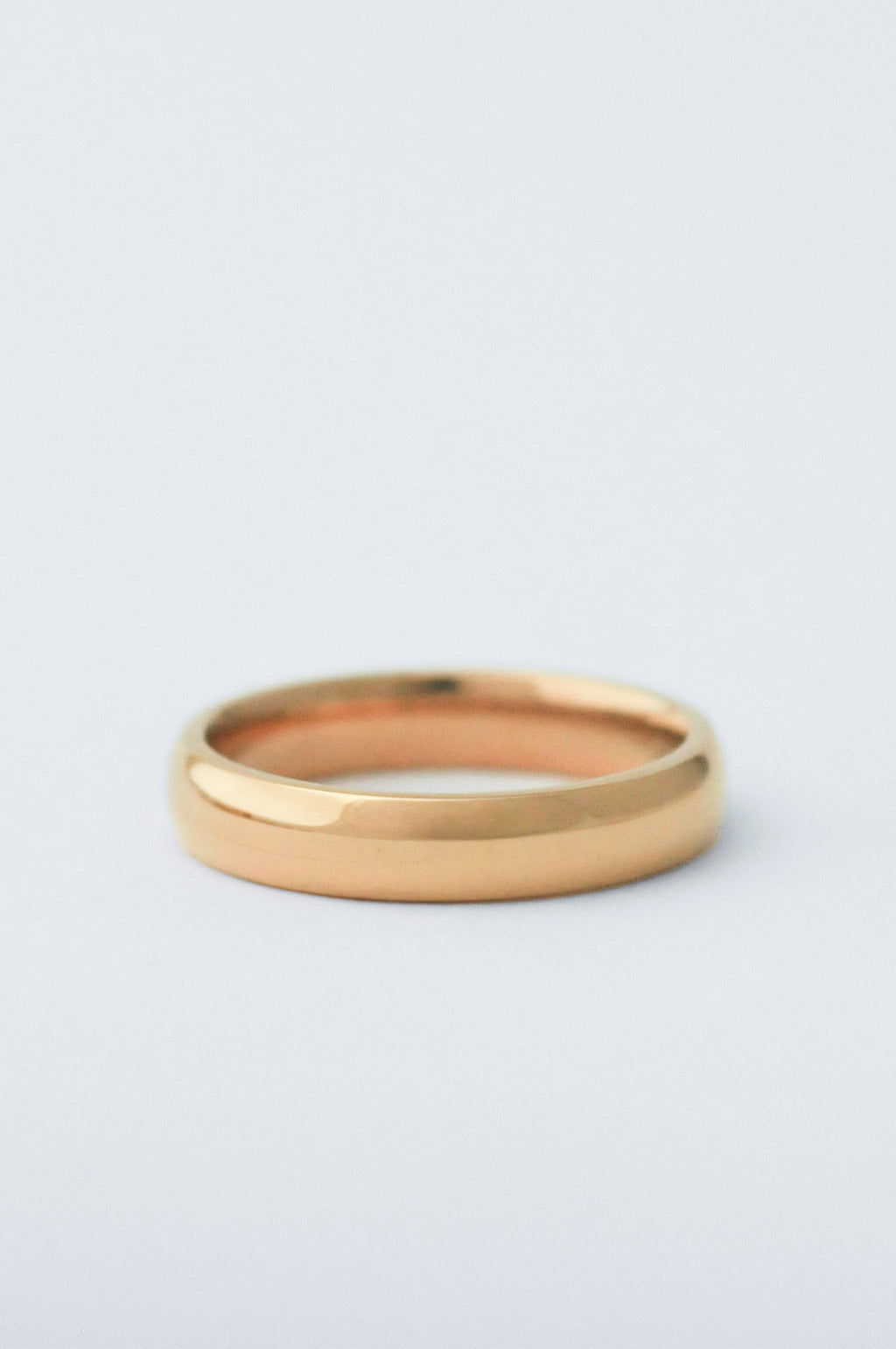 A minimalist, polished yellow gold band ring photographed on a clean, light gray background.