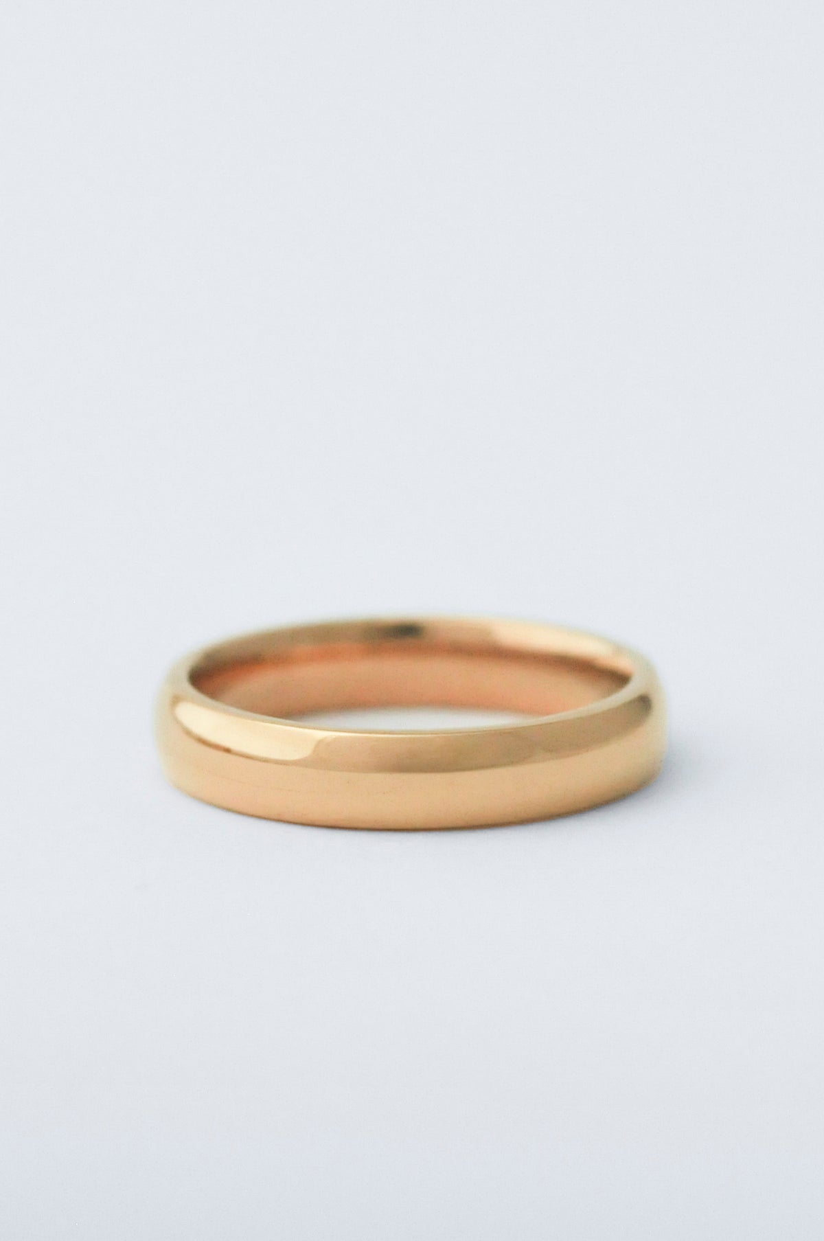 A minimalist, polished yellow gold band ring photographed on a clean, light gray background.