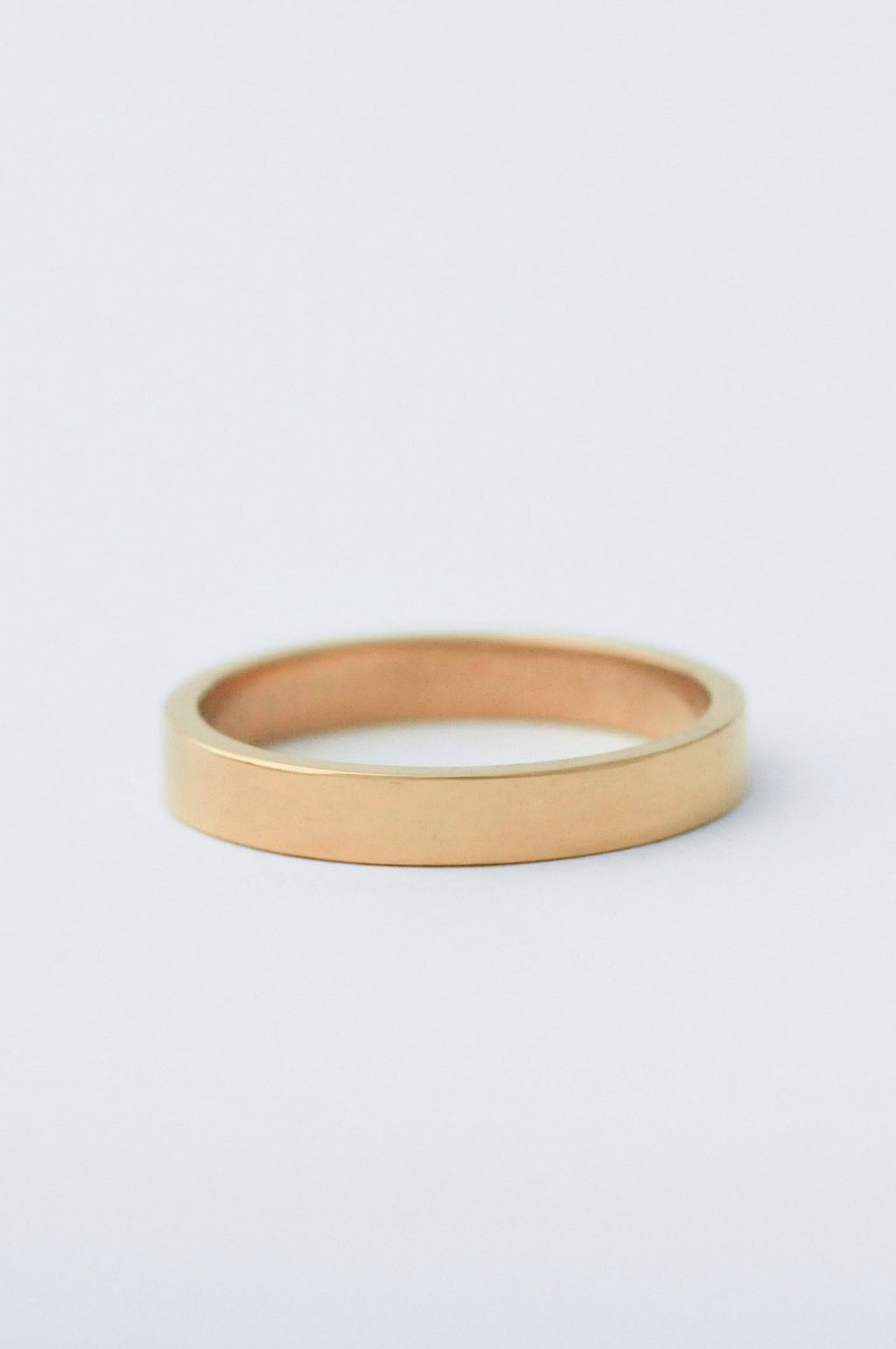 A minimalist, polished yellow gold band ring photographed on a clean, light gray background.