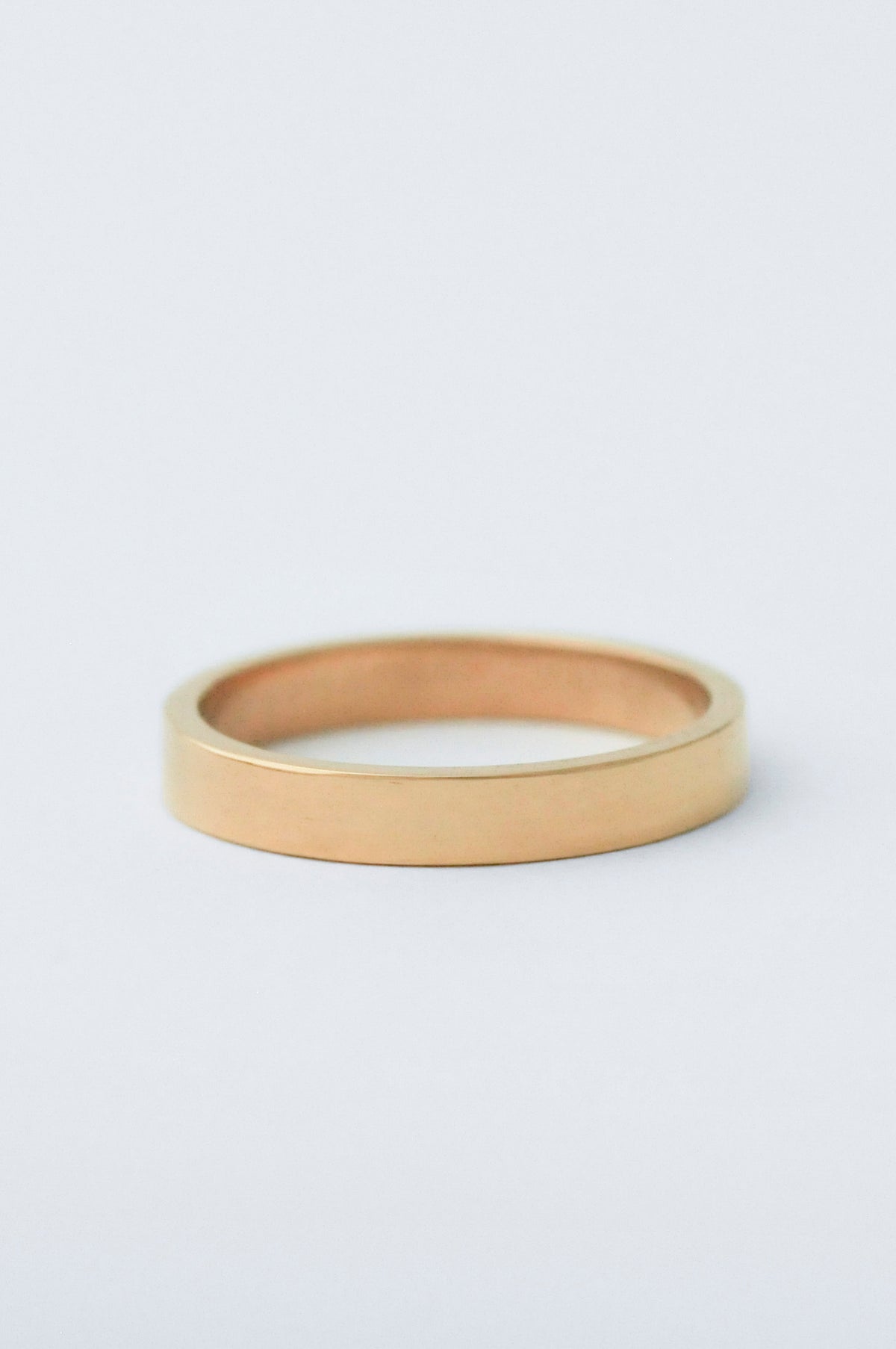 A minimalist, polished yellow gold band ring photographed on a clean, light gray background.