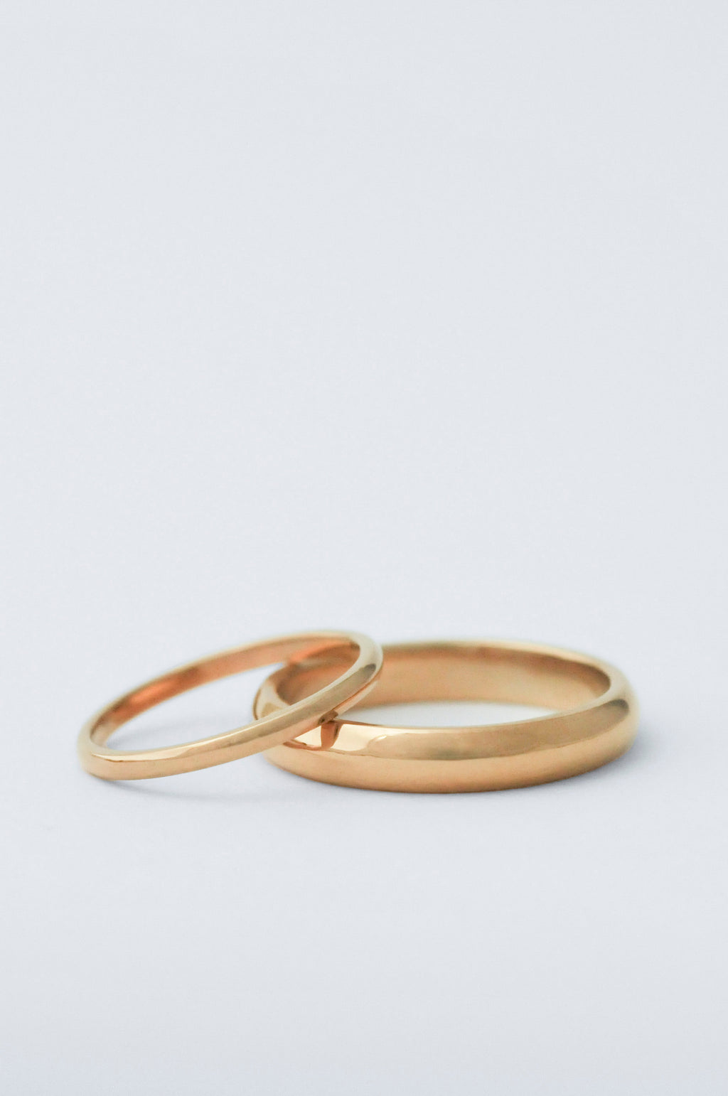 two court wedding bands staggered on top of each other. The bottom ring is 5mm thick and the top one is 2mm both in yellow gold