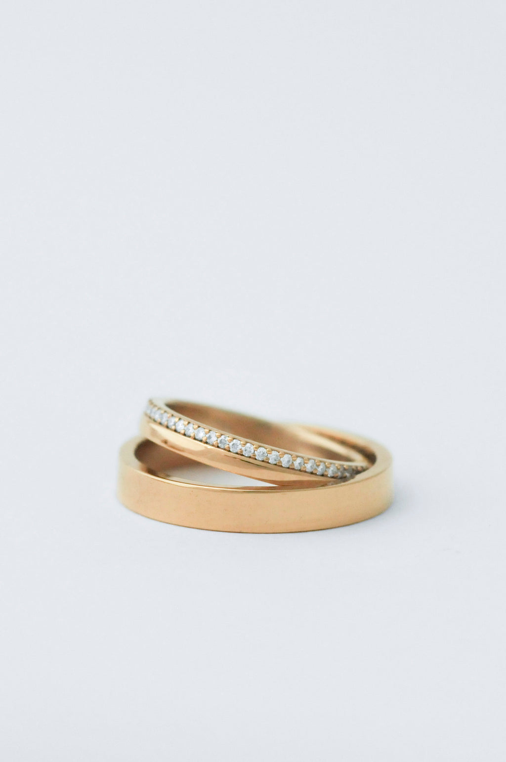 A pair of gold rings, one smooth and one pavé-set with small clear stones, photographed on a clean white background.