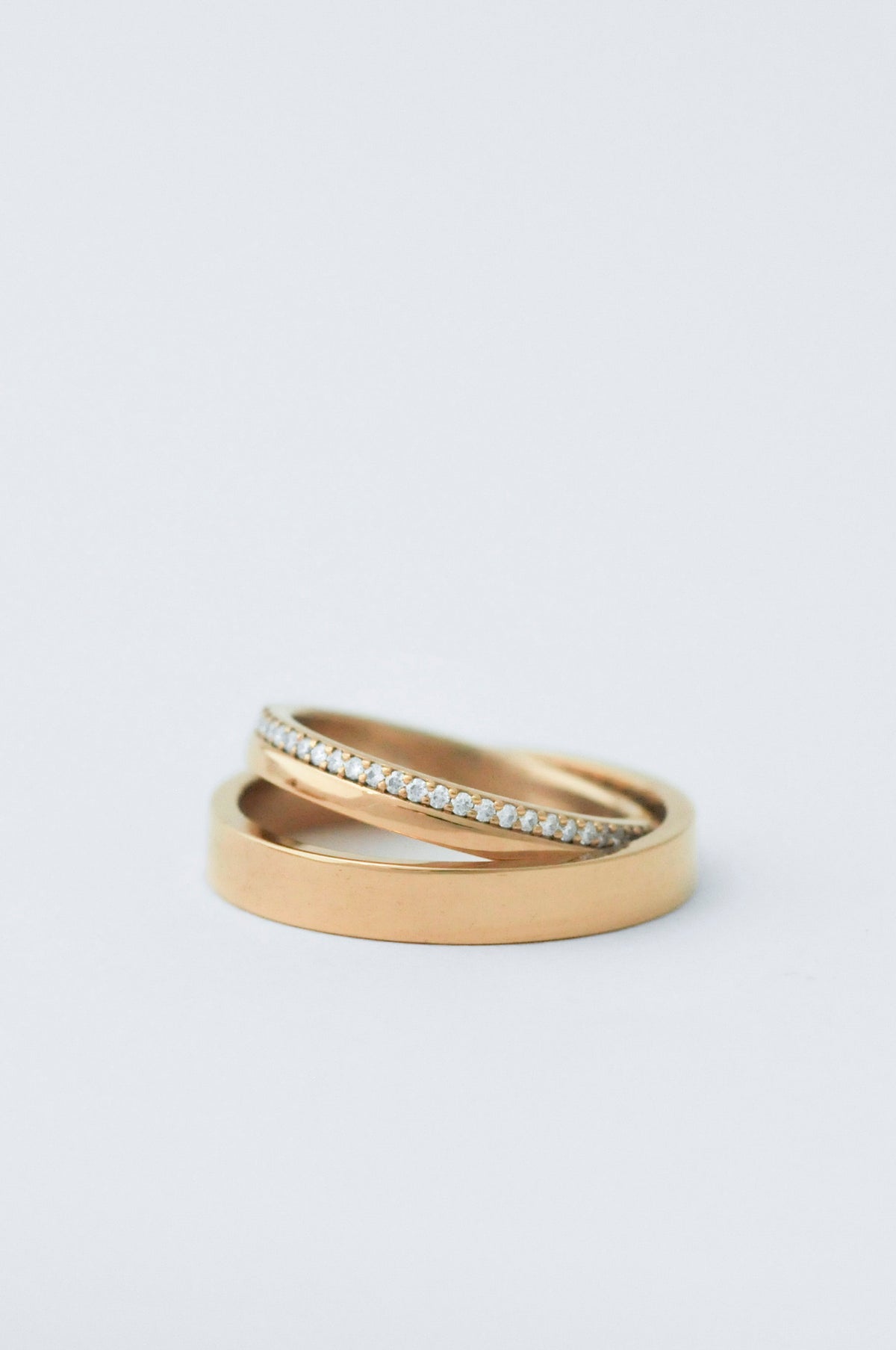 A pair of gold rings, one smooth and one pavé-set with small clear stones, photographed on a clean white background.