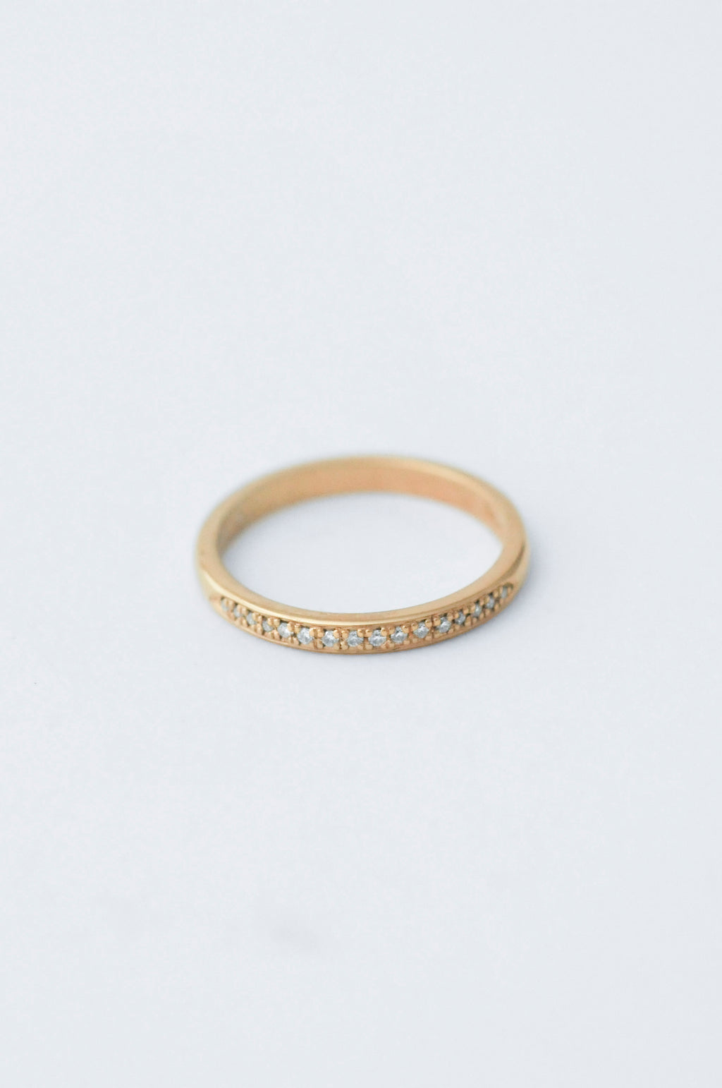 A thin yellow gold eternity ring with a row of small clear pavé gemstones along the front band, photographed on a clean white background.