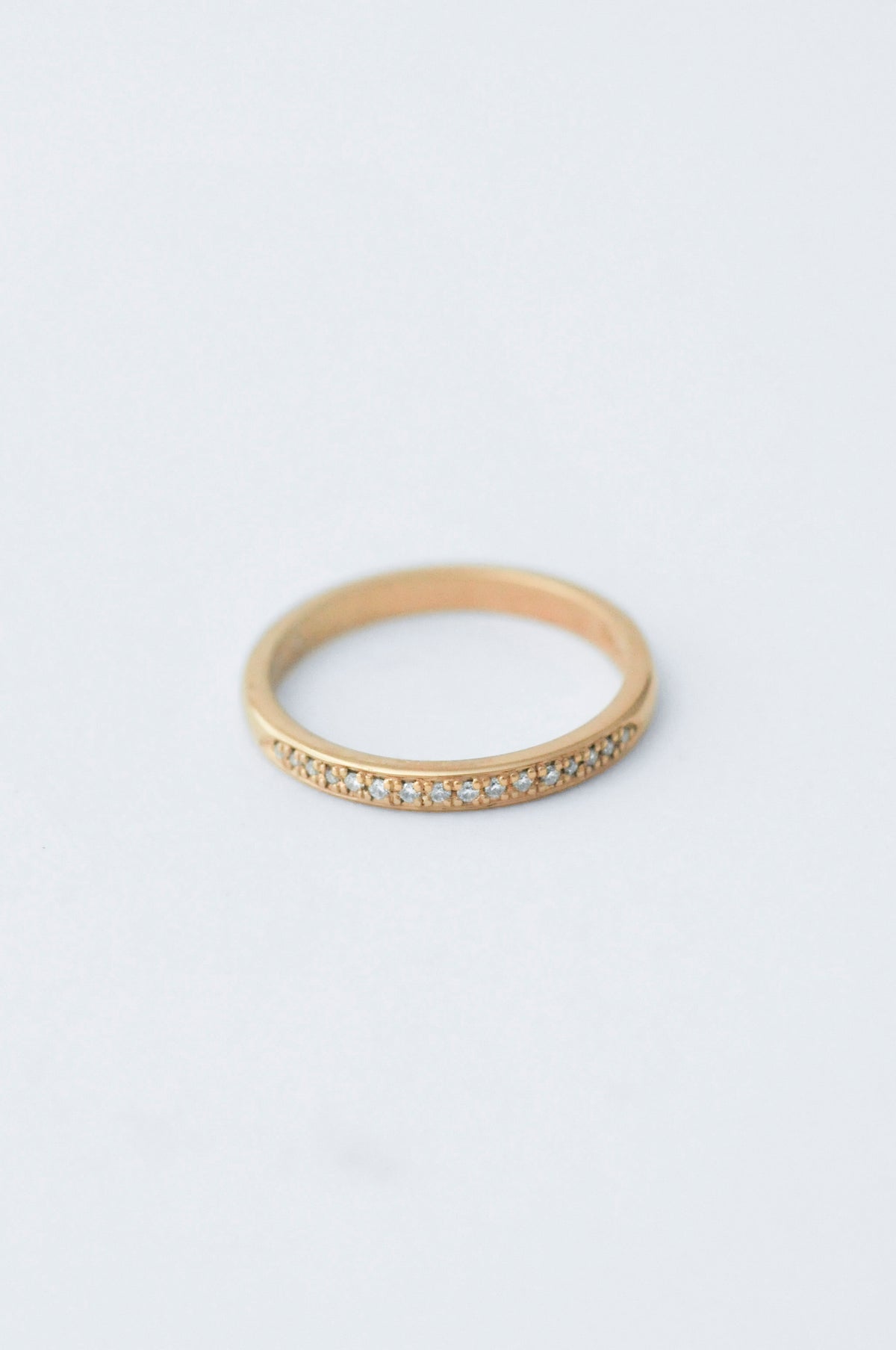 A thin yellow gold eternity ring with a row of small clear pavé gemstones along the front band, photographed on a clean white background.