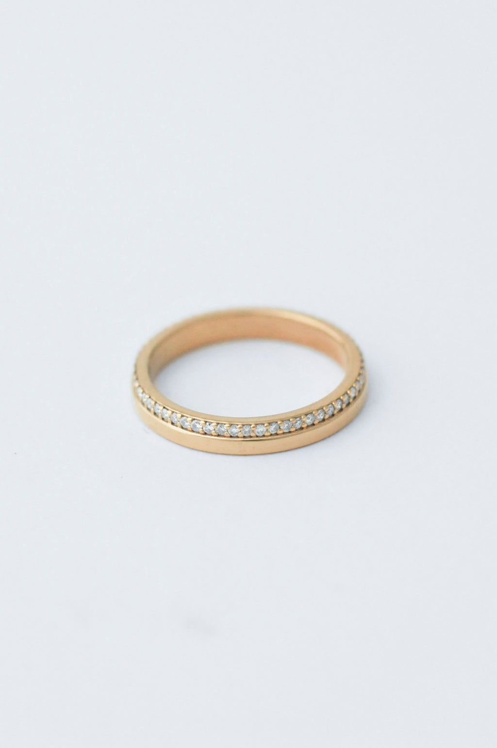 A thin gold eternity ring with a row of small clear stones on one side, photographed on a clean white background.