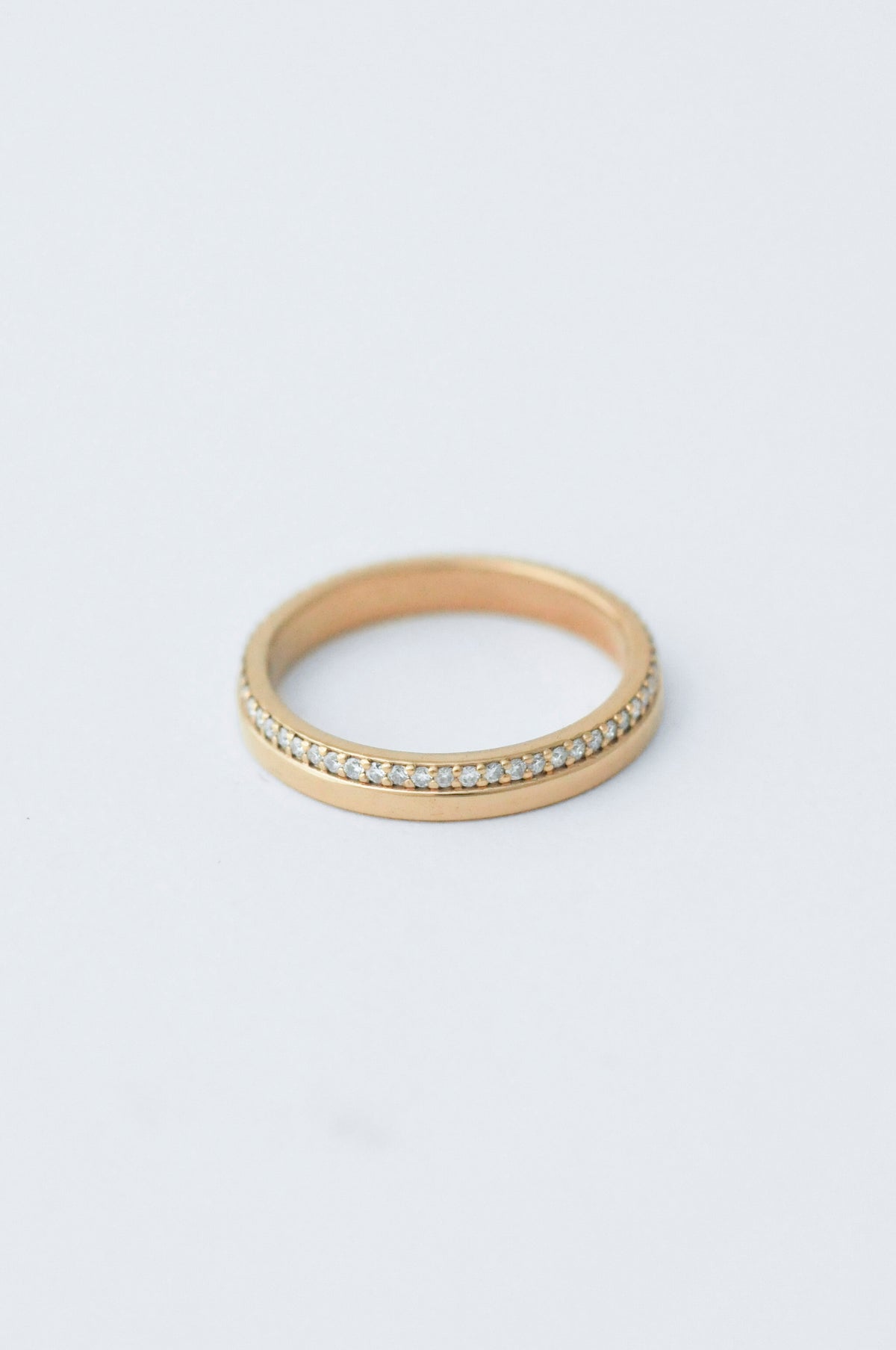 A thin gold eternity ring with a row of small clear stones on one side, photographed on a clean white background.