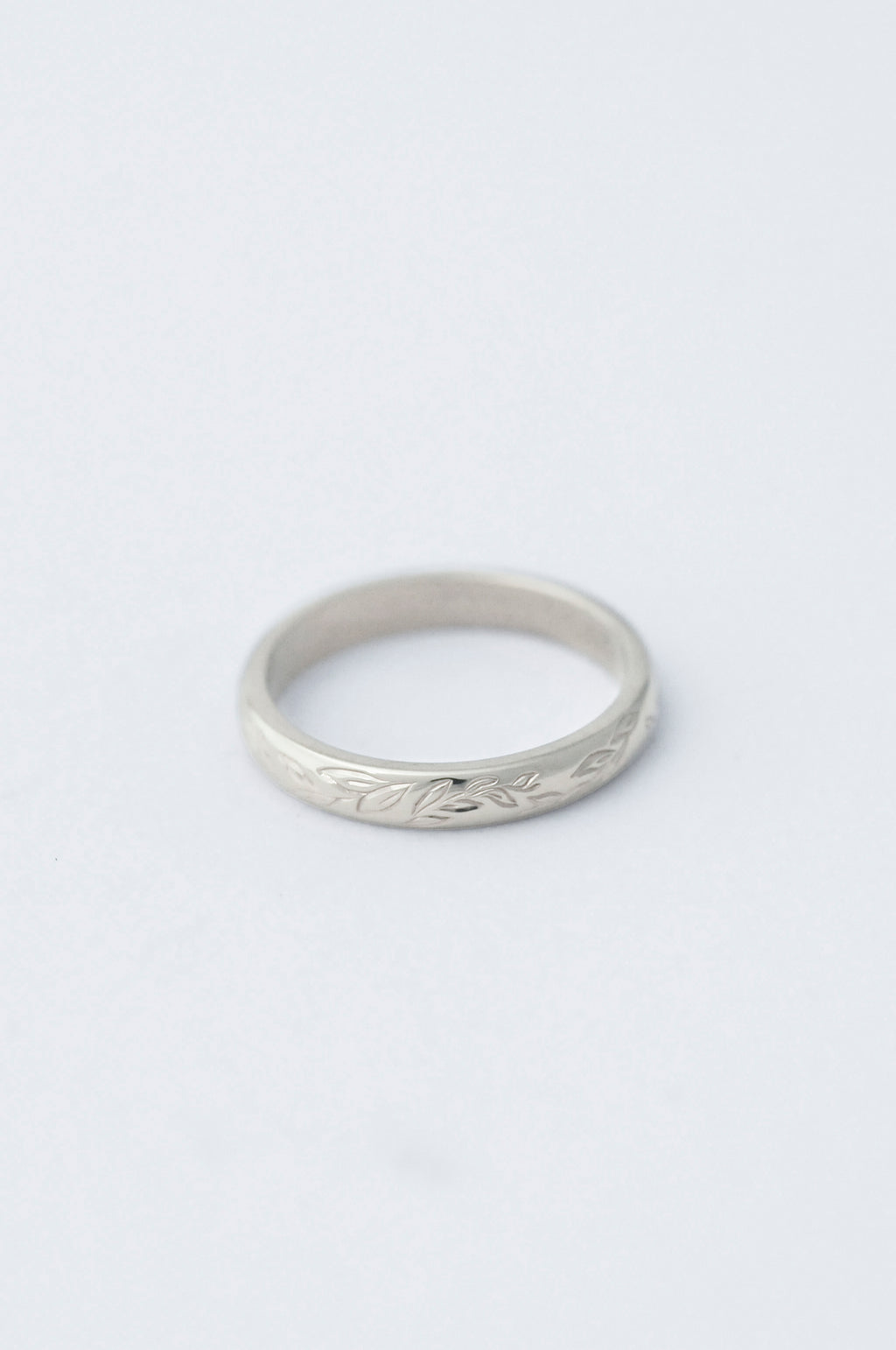 platinum wedding band ring with willow leaf hand engraved detailing on a light grey background