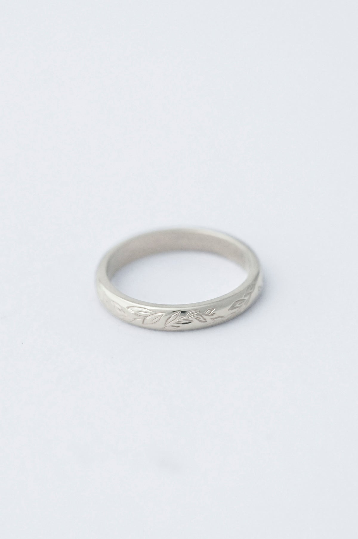 platinum wedding band ring with willow leaf hand engraved detailing on a light grey background